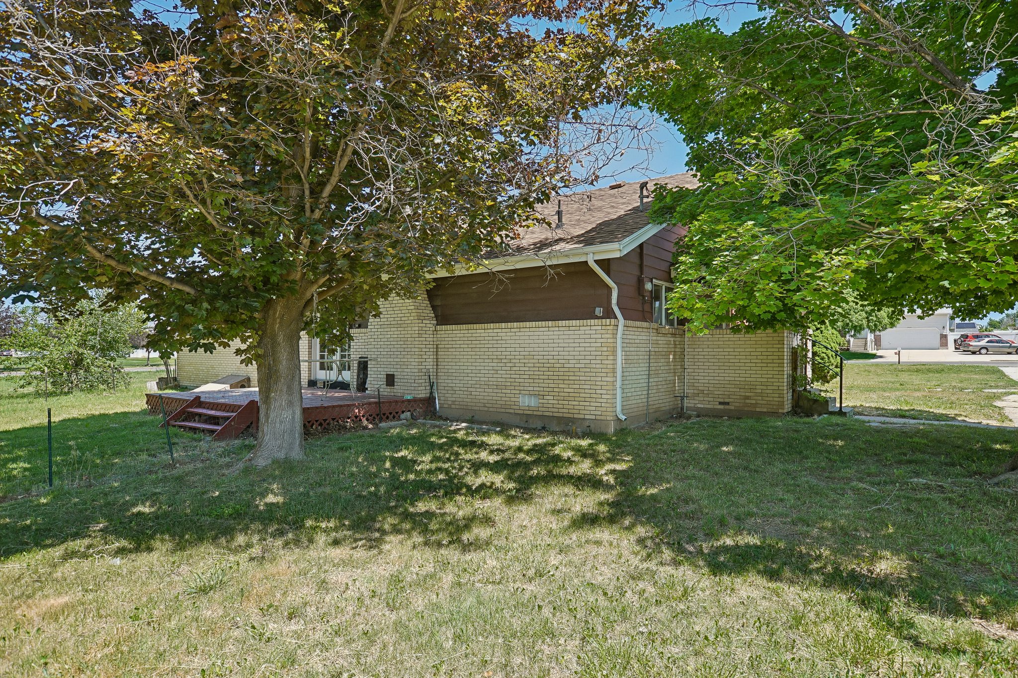 Expansive backyard featuring a large tree, a raised wood deck with steps, and a light-colored brick exterior