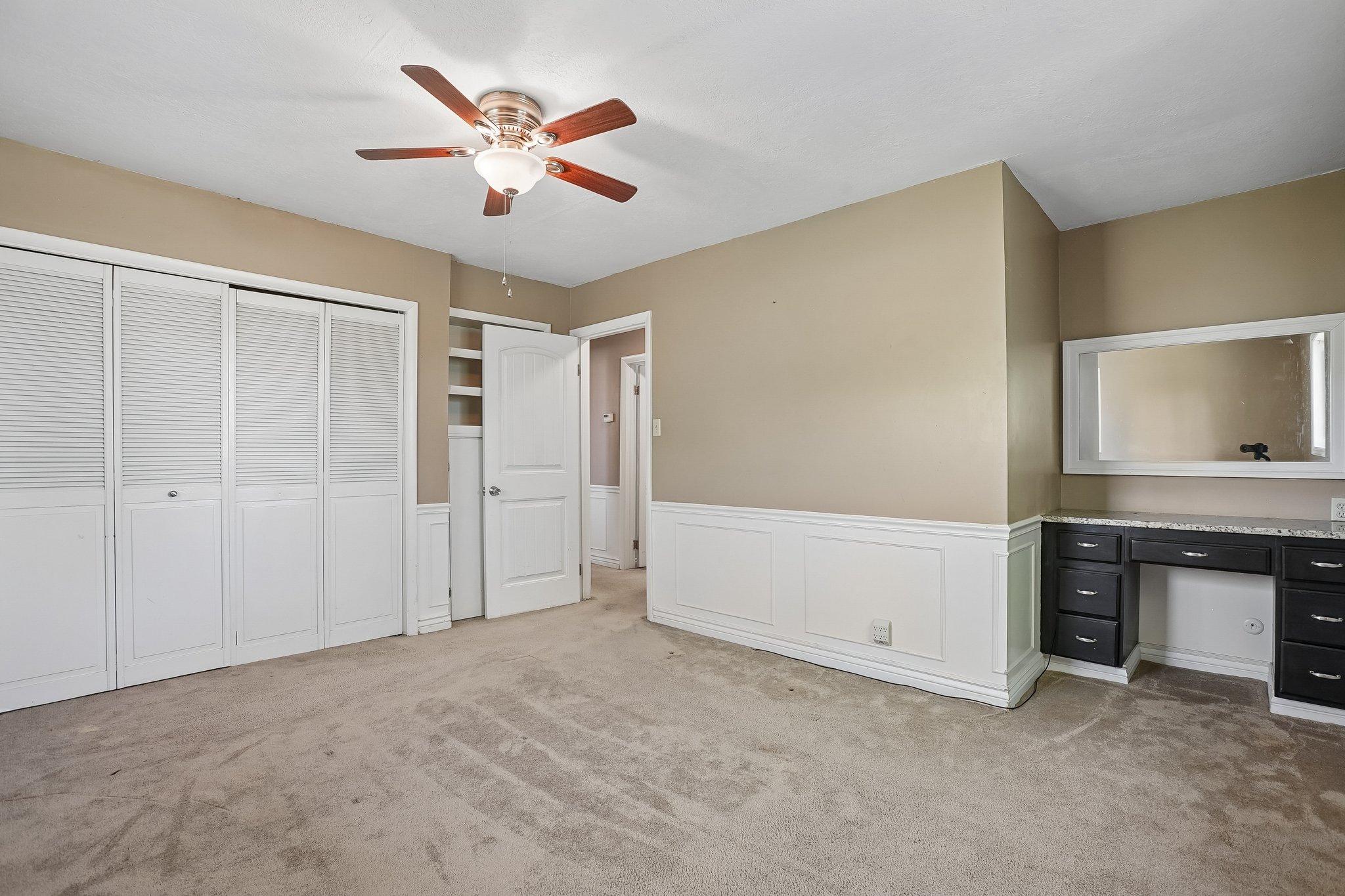 Neutral-toned room featuring a wood-finish ceiling fan with integrated lighting, extensive wainscoting, and carpet flooring
