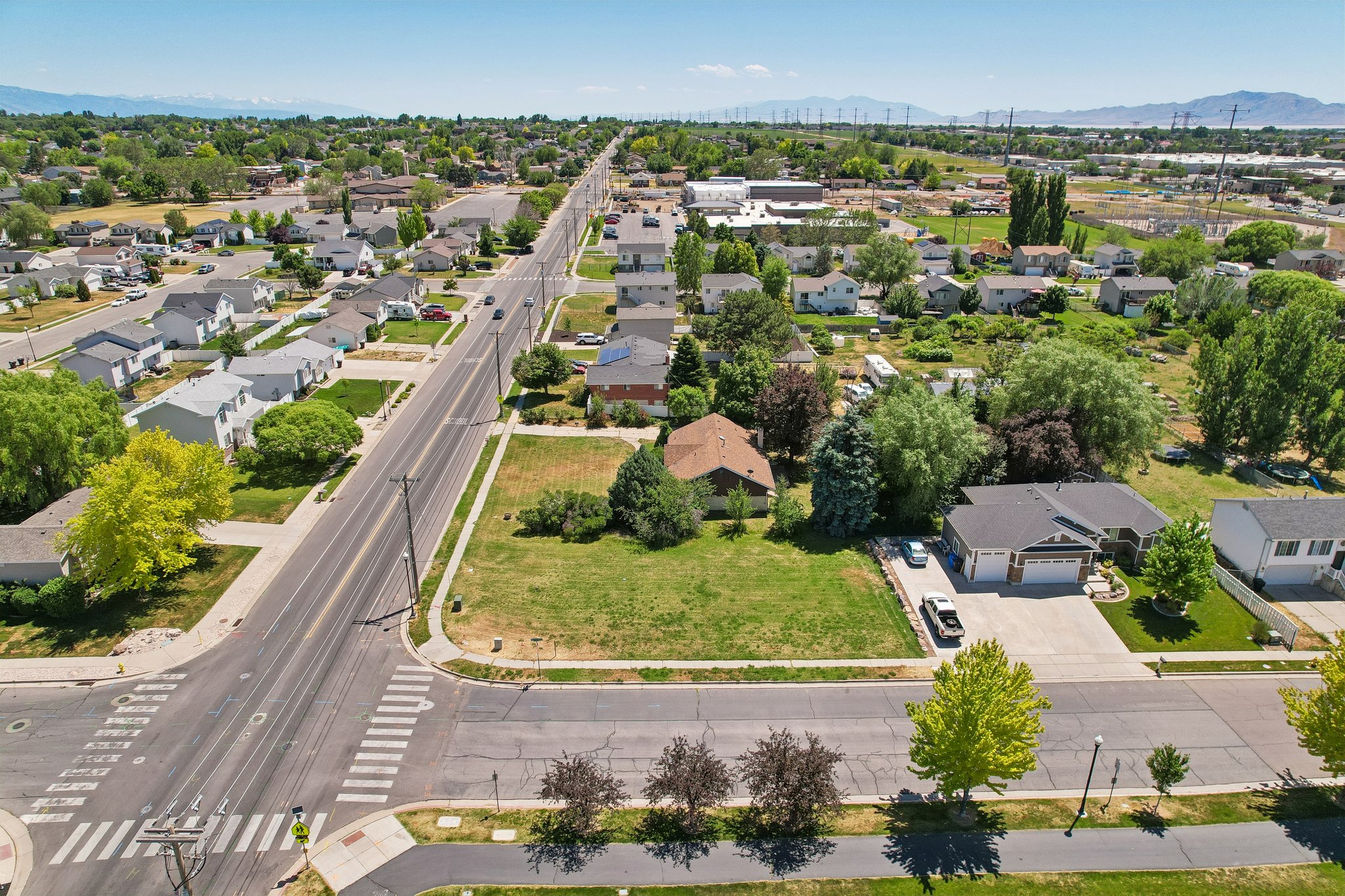 Expansive corner lot featuring mature trees and a paved street with crosswalk access