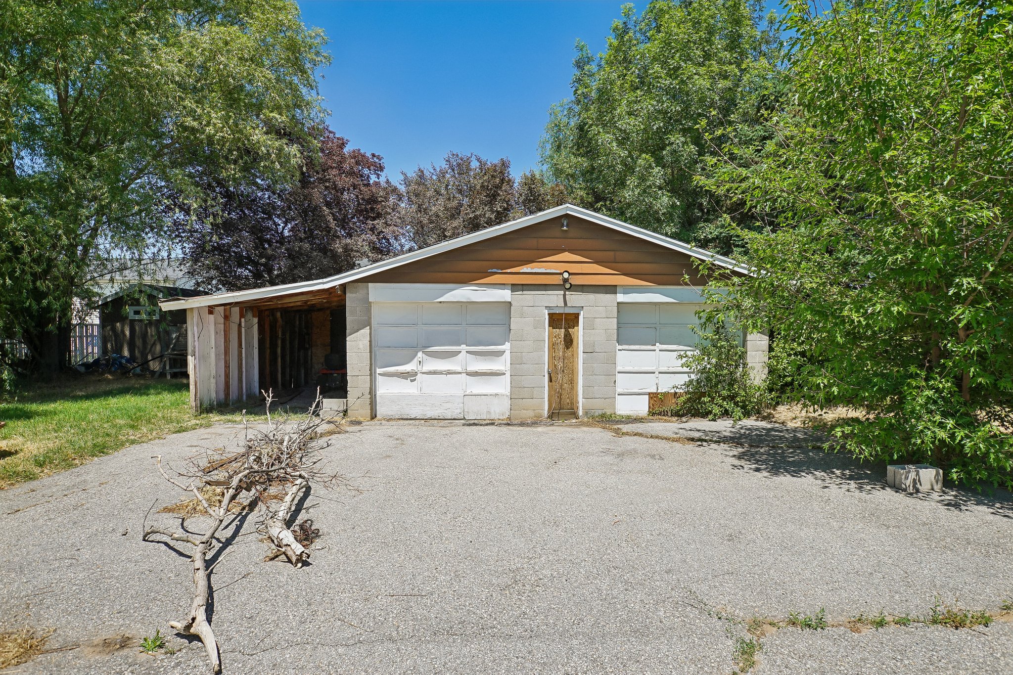 Structure featuring a two-car garage with white doors, a central wooden entry door, and a brown siding gable