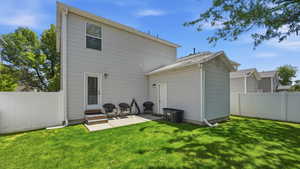 Rear exterior featuring a manicured lawn, white vinyl fencing, a concrete patio, and a side entrance door