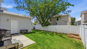 Expansive backyard featuring a manicured lawn, a concrete patio, a mature shade tree, a white vinyl privacy fence, and a raised garden bed