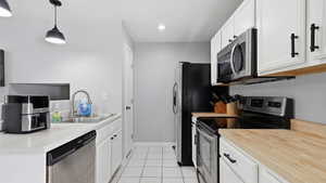 Galley kitchen featuring white cabinetry with matte black hardware, stainless steel appliances, a double basin sink, and pendant lighting
