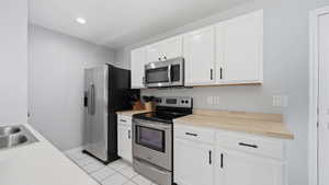 Kitchen featuring white cabinetry with matte black hardware, stainless steel appliances, wood-finish countertops, and white tile flooring