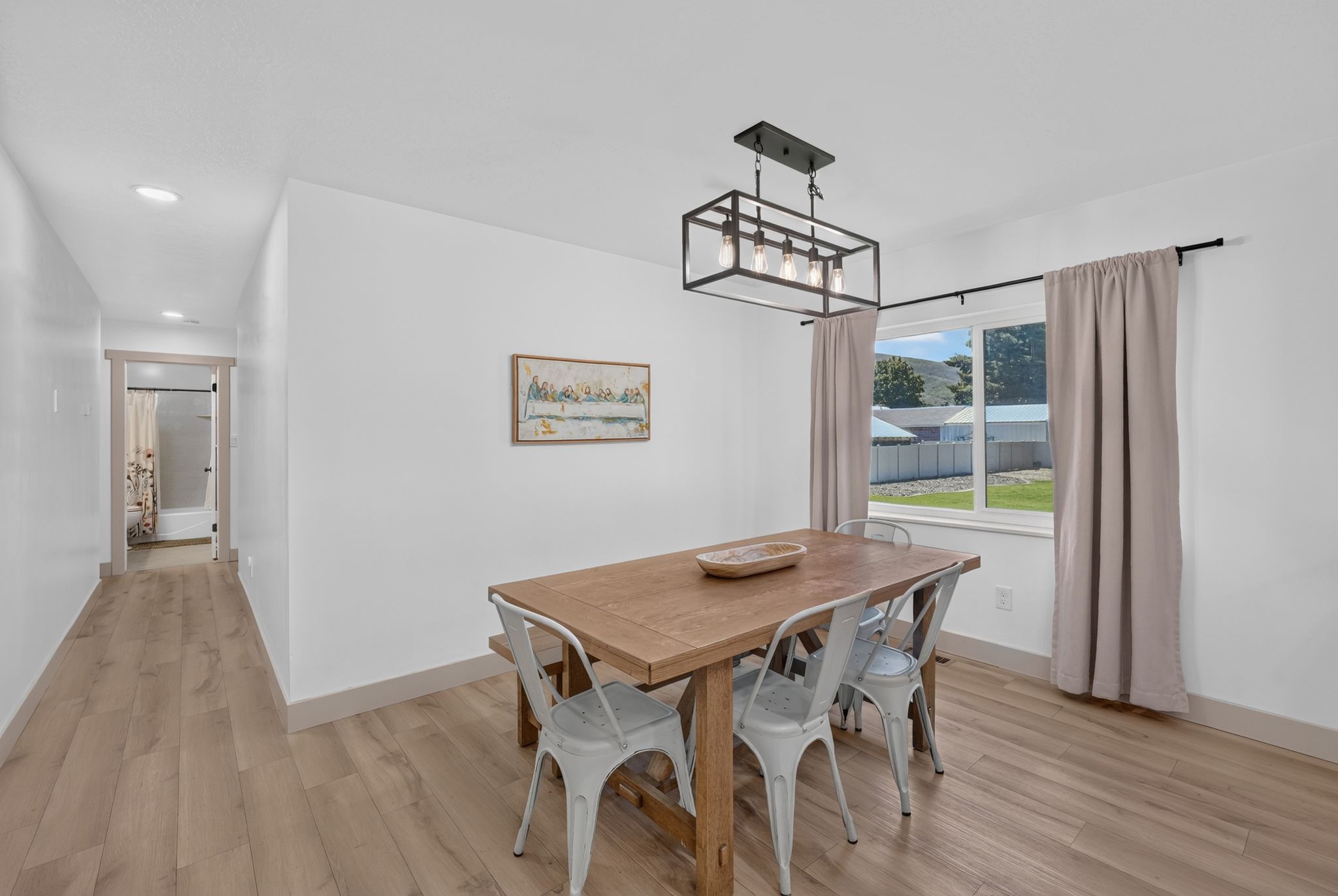 Spacious dining area featuring wood-finish flooring, a contemporary black metal and glass chandelier, and a large window with natural light