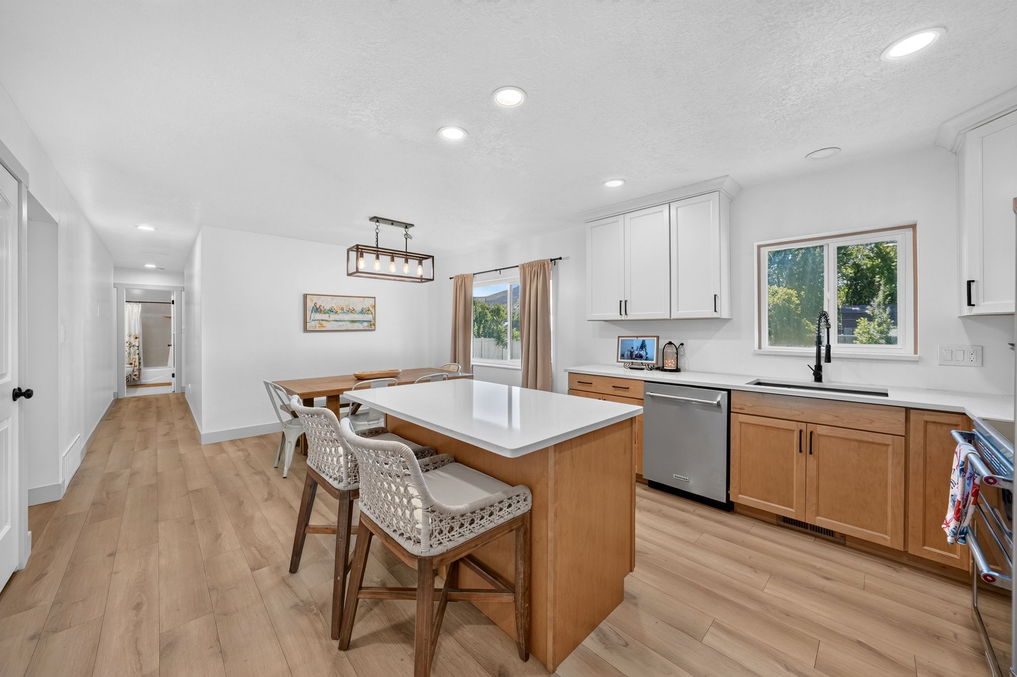 Open-concept kitchen featuring an island with a light-toned countertop, wood-finish flooring, white upper cabinetry, natural wood lower cabinetry, and recessed lighting