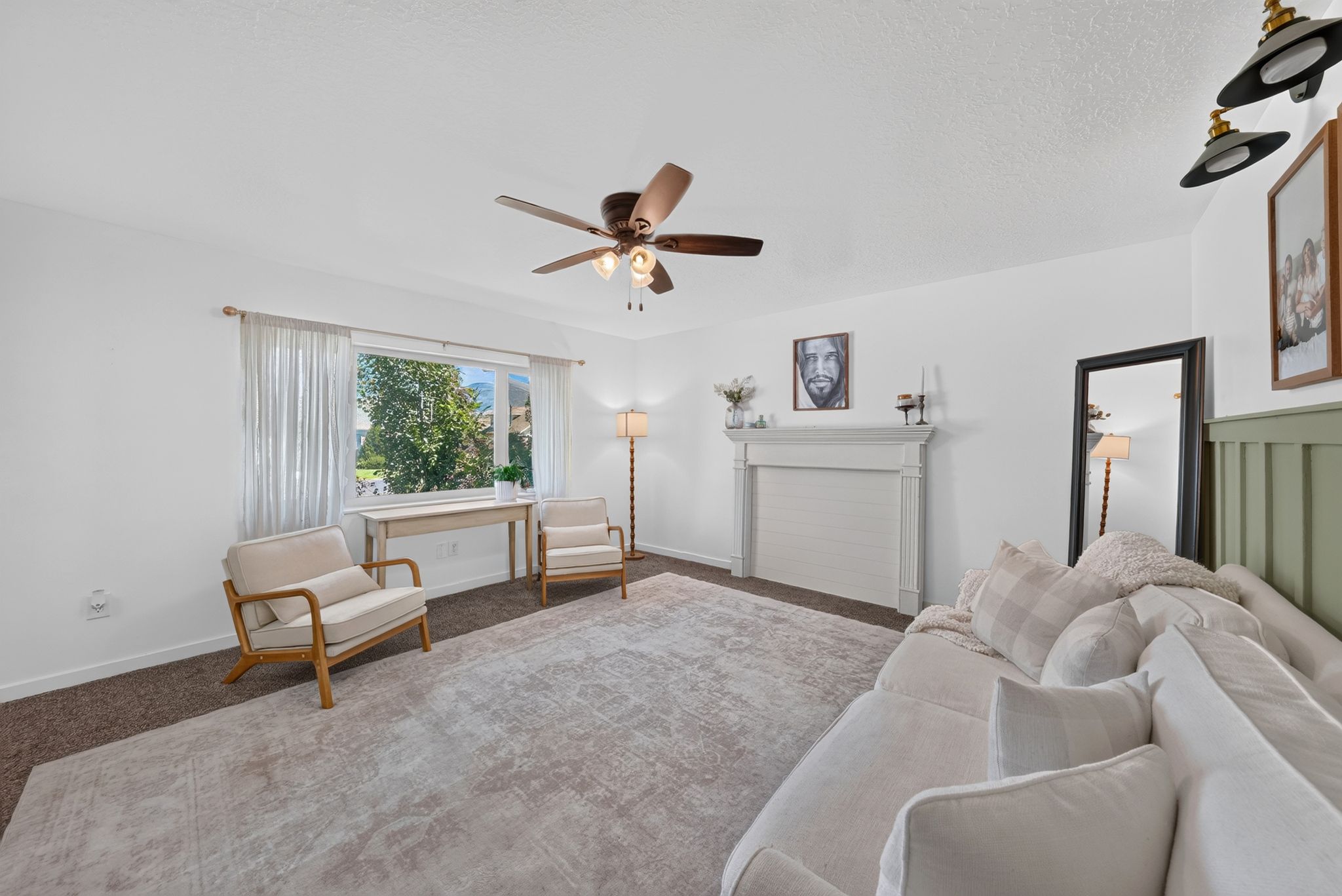 Spacious interior featuring a decorative mantel, broad window, ceiling fan with light fixture, and neutral wall tones