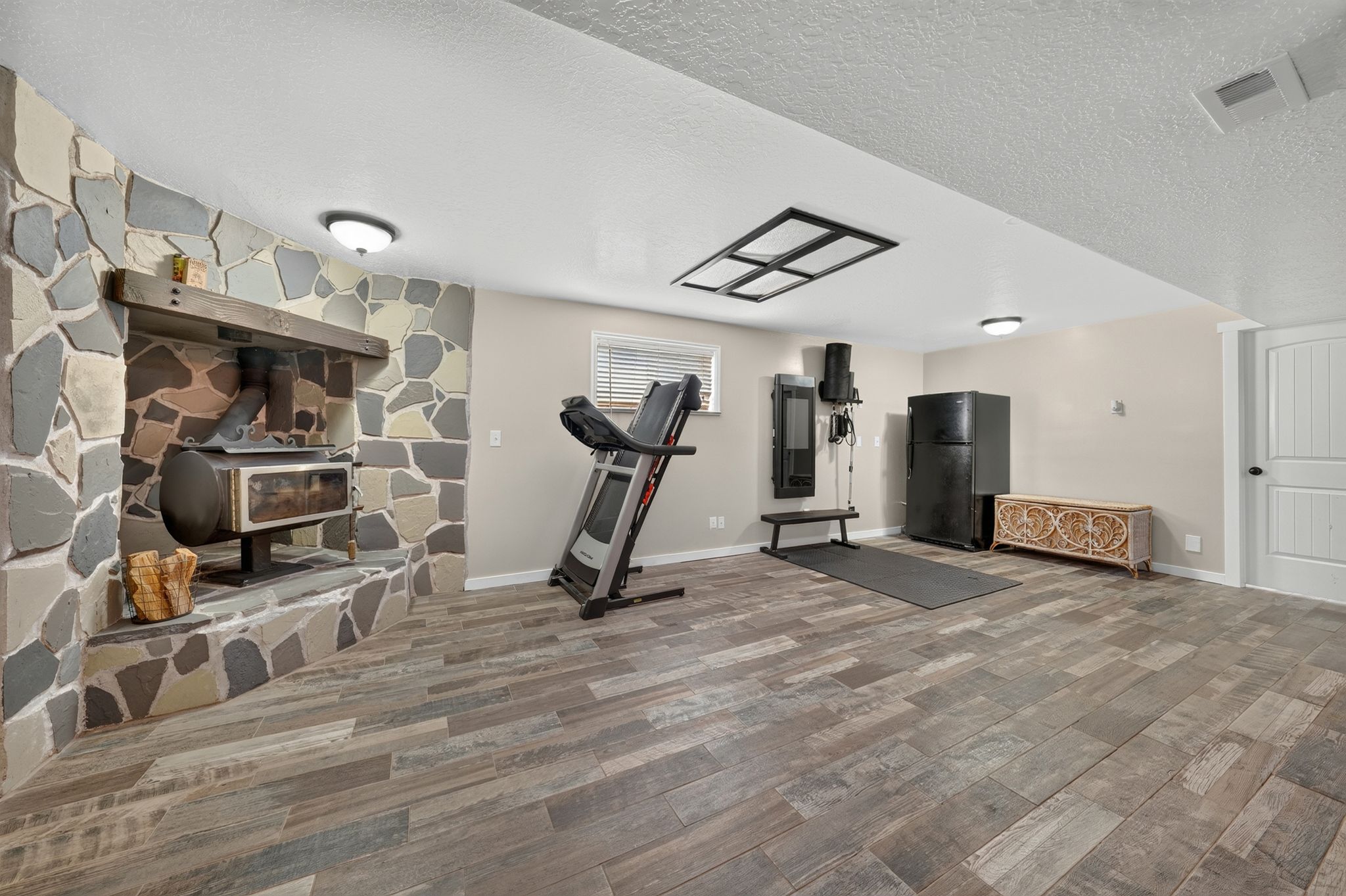 Spacious Recreation room featuring a stone-clad fireplace with a wood-burning stove, wood-finish flooring, recessed lighting, and a white paneled door