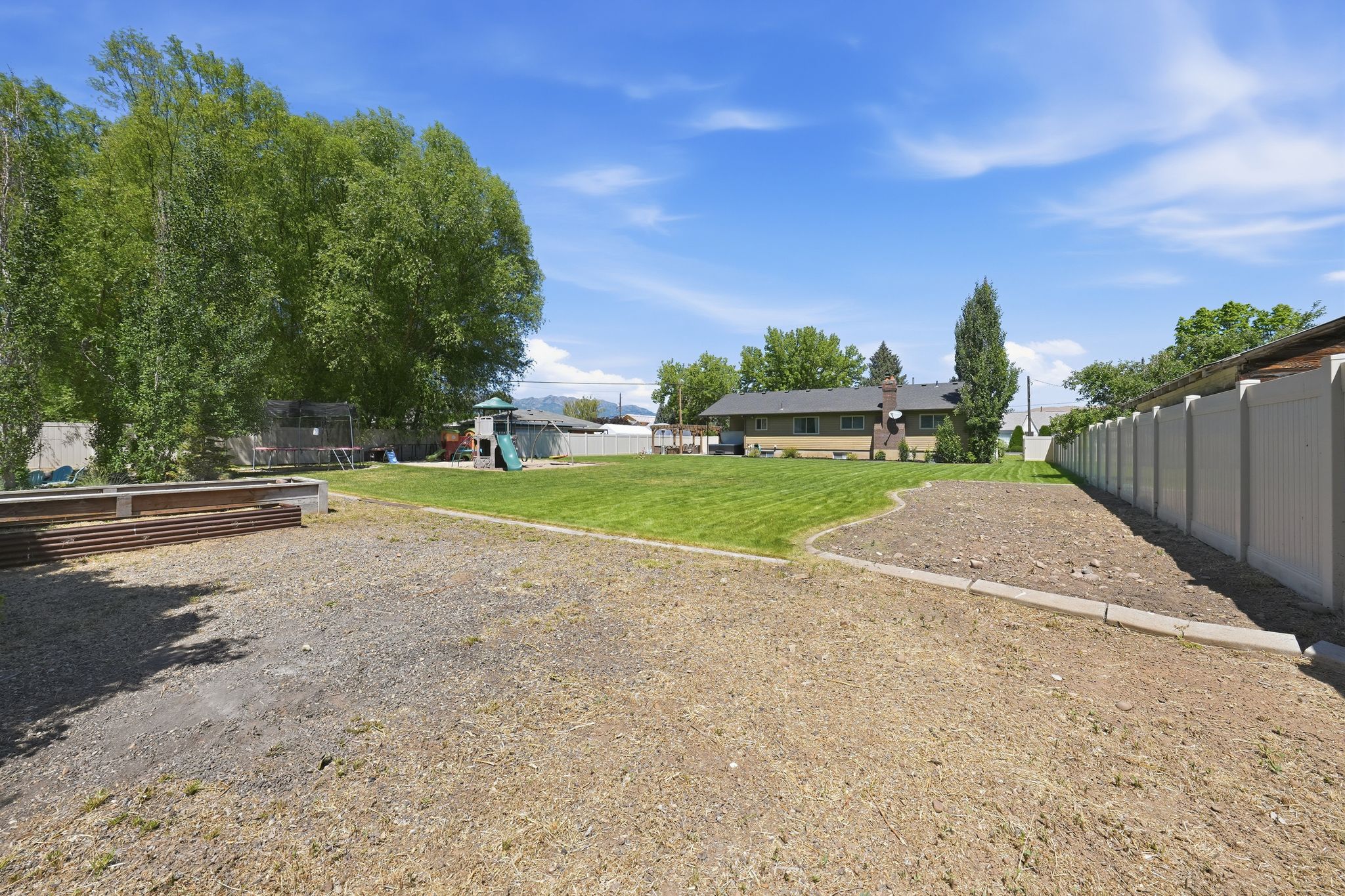 Expansive property featuring a large grassy area, mature trees, a designated garden space, and a tall privacy fence