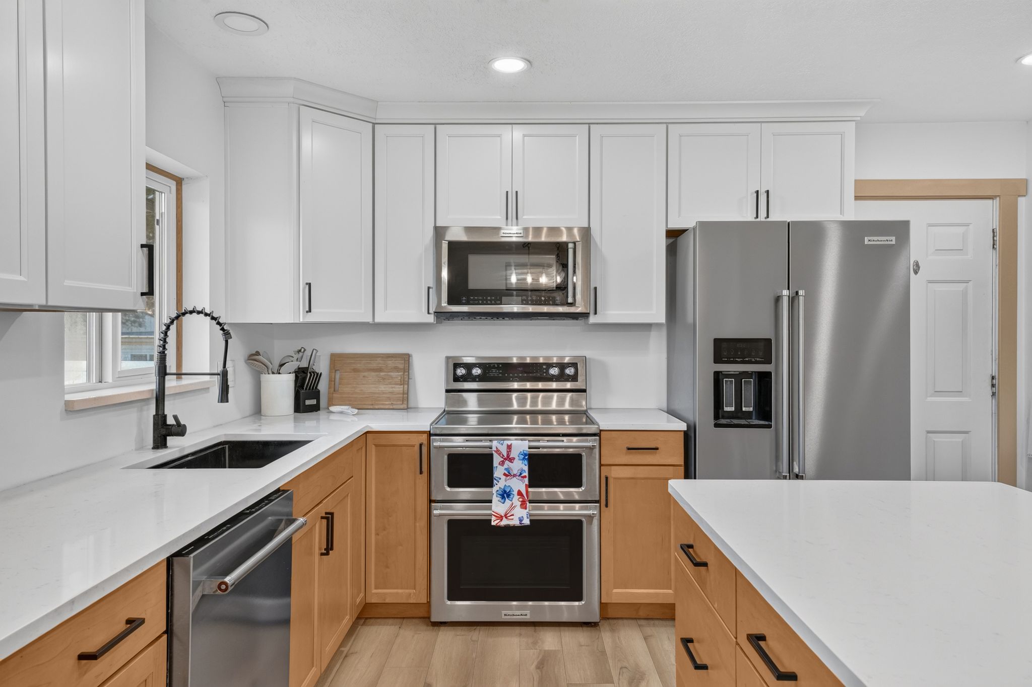 Contemporary kitchen featuring two-tone cabinetry, stainless steel appliances, white countertops, and wood-finish flooring