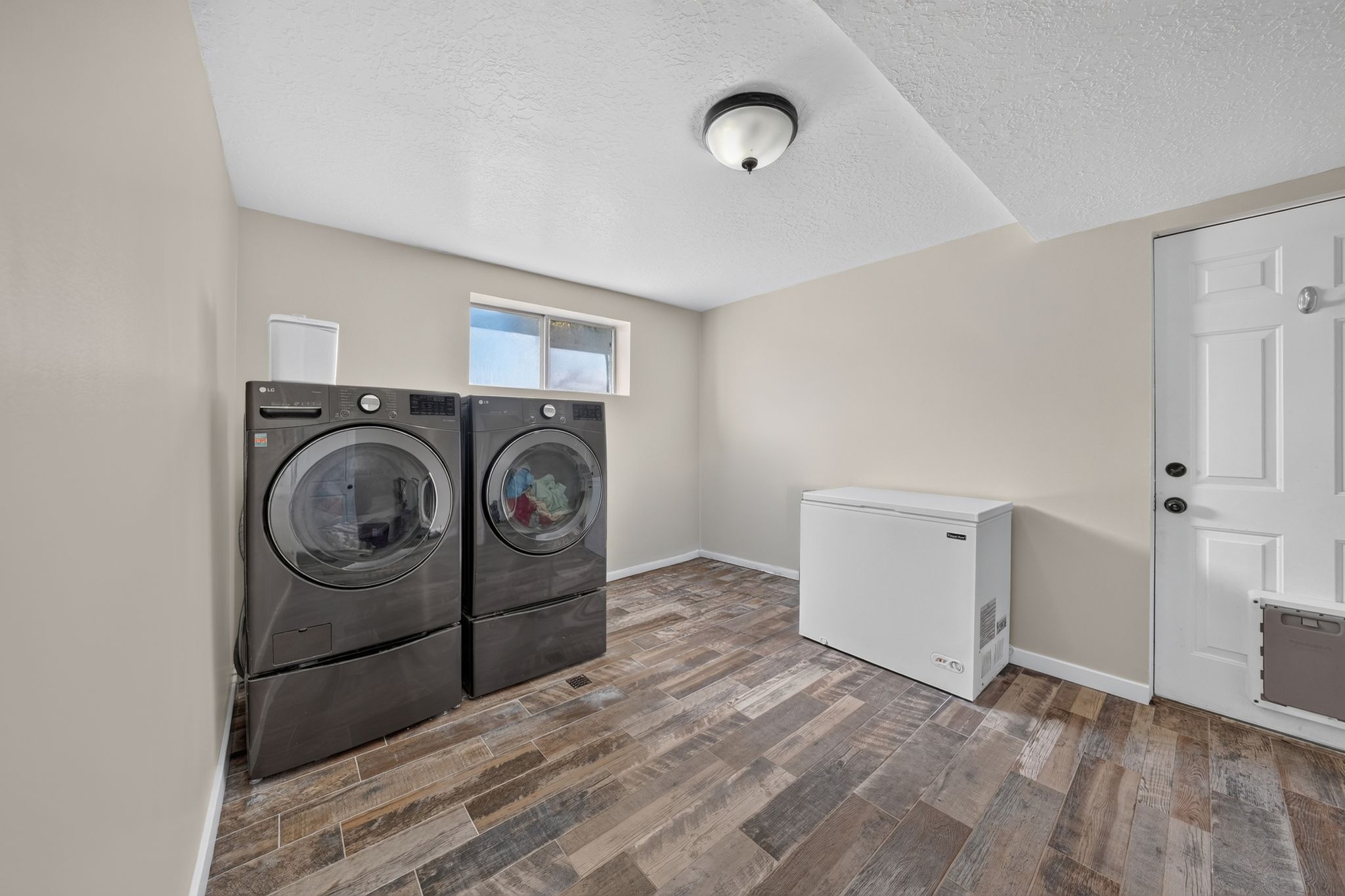 Dedicated laundry area featuring wood-finish flooring, light neutral walls, and a ceiling-mounted light fixture