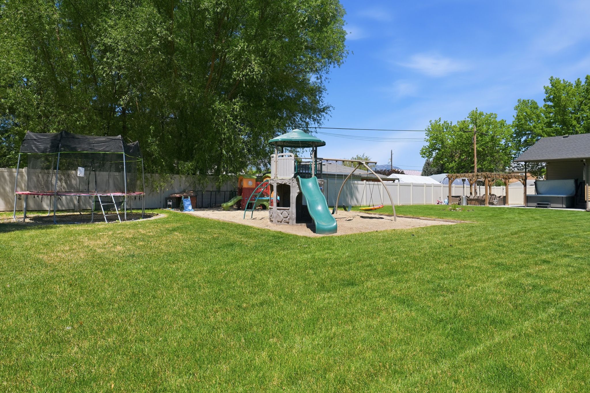 Expansive lawn area featuring a sand play zone, covered patio, and a privacy fence