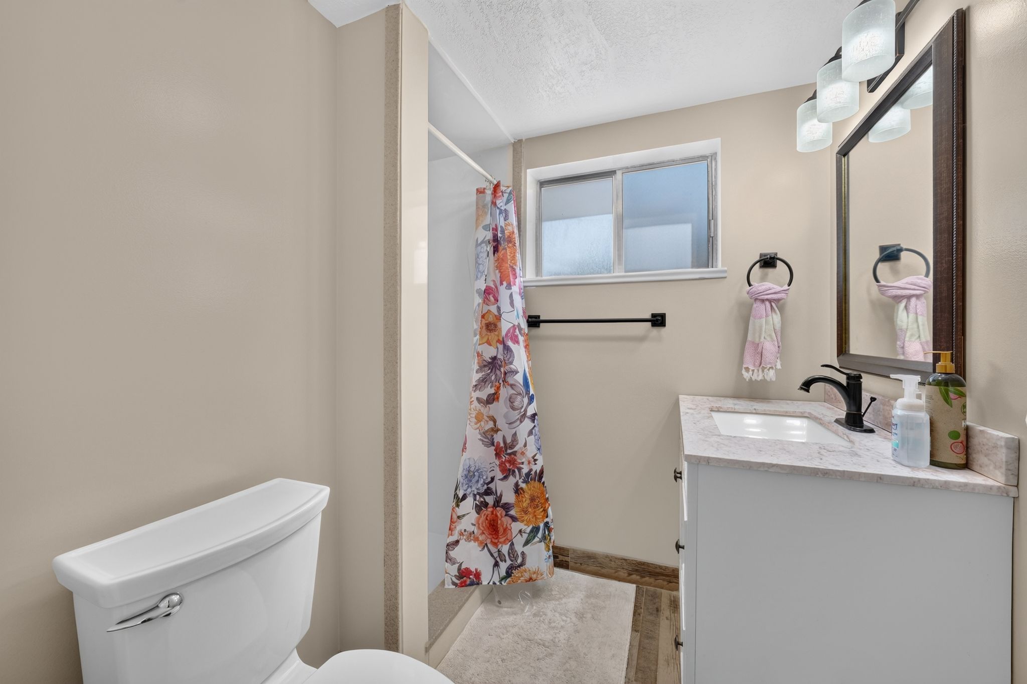 Bathroom featuring a single vanity with a white countertop and undermount sink, black-finish faucet, and coordinating framed mirror