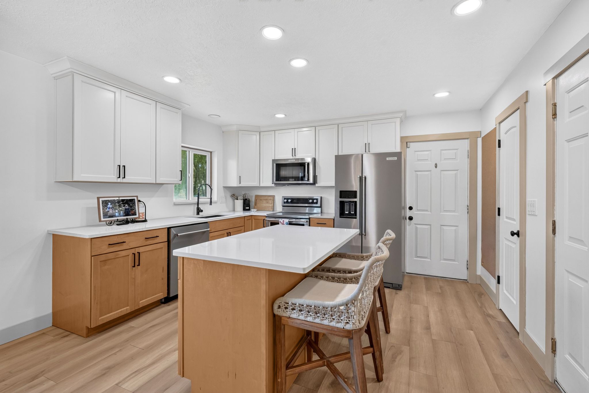 Kitchen featuring two-tone cabinetry, stainless steel appliances, a center island with countertop seating, recessed lighting, and wood-finish flooring