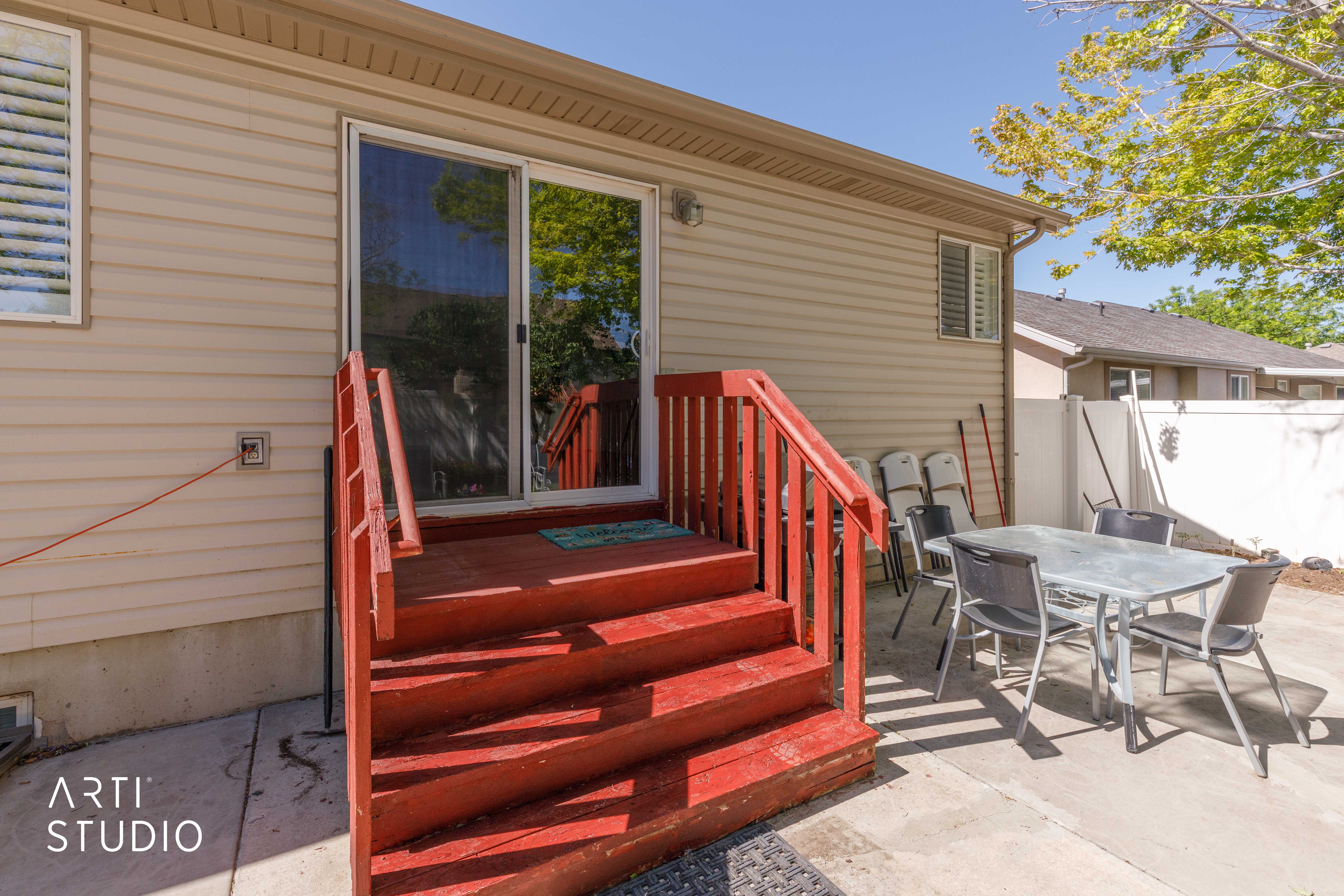 Concrete patio featuring a red-stained wood deck with stairs and railings, vinyl siding, and a sliding glass door