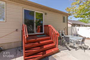 Concrete patio featuring a red-stained wood deck with stairs and railings, vinyl siding, and a sliding glass door