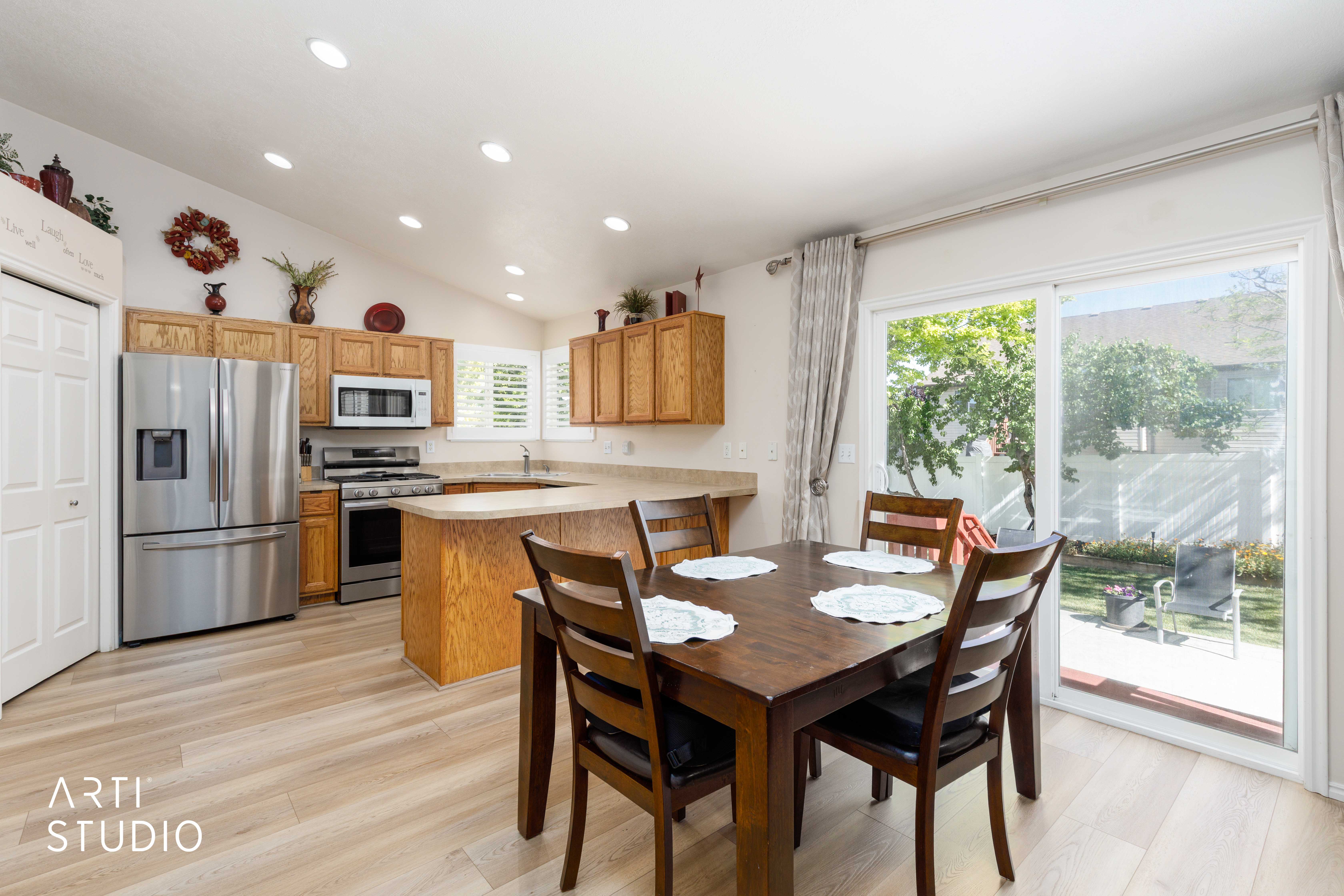 Open-concept kitchen and dining area featuring light wood-finish flooring, vaulted ceilings with recessed lighting, and a stainless steel appliance suite