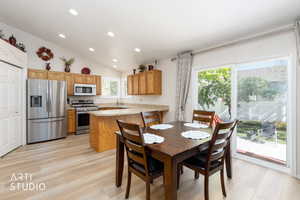 Open-concept kitchen and dining area featuring light wood-finish flooring, vaulted ceilings with recessed lighting, and a stainless steel appliance suite