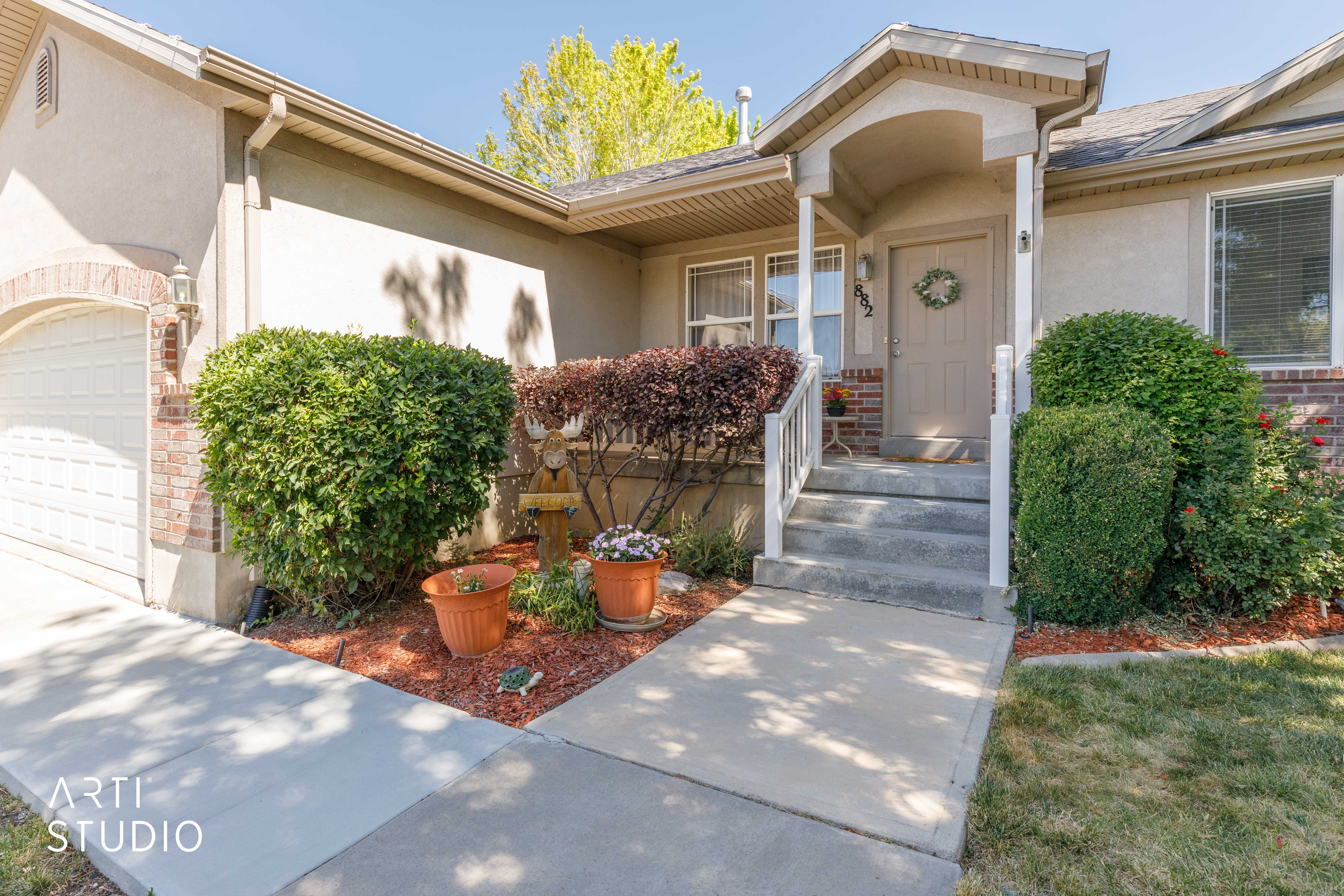 Exterior featuring stucco siding, brick accents, a covered entry with white railings, a concrete pathway, and mature landscaping
