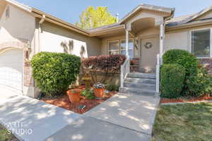 Exterior featuring stucco siding, brick accents, a covered entry with white railings, a concrete pathway, and mature landscaping