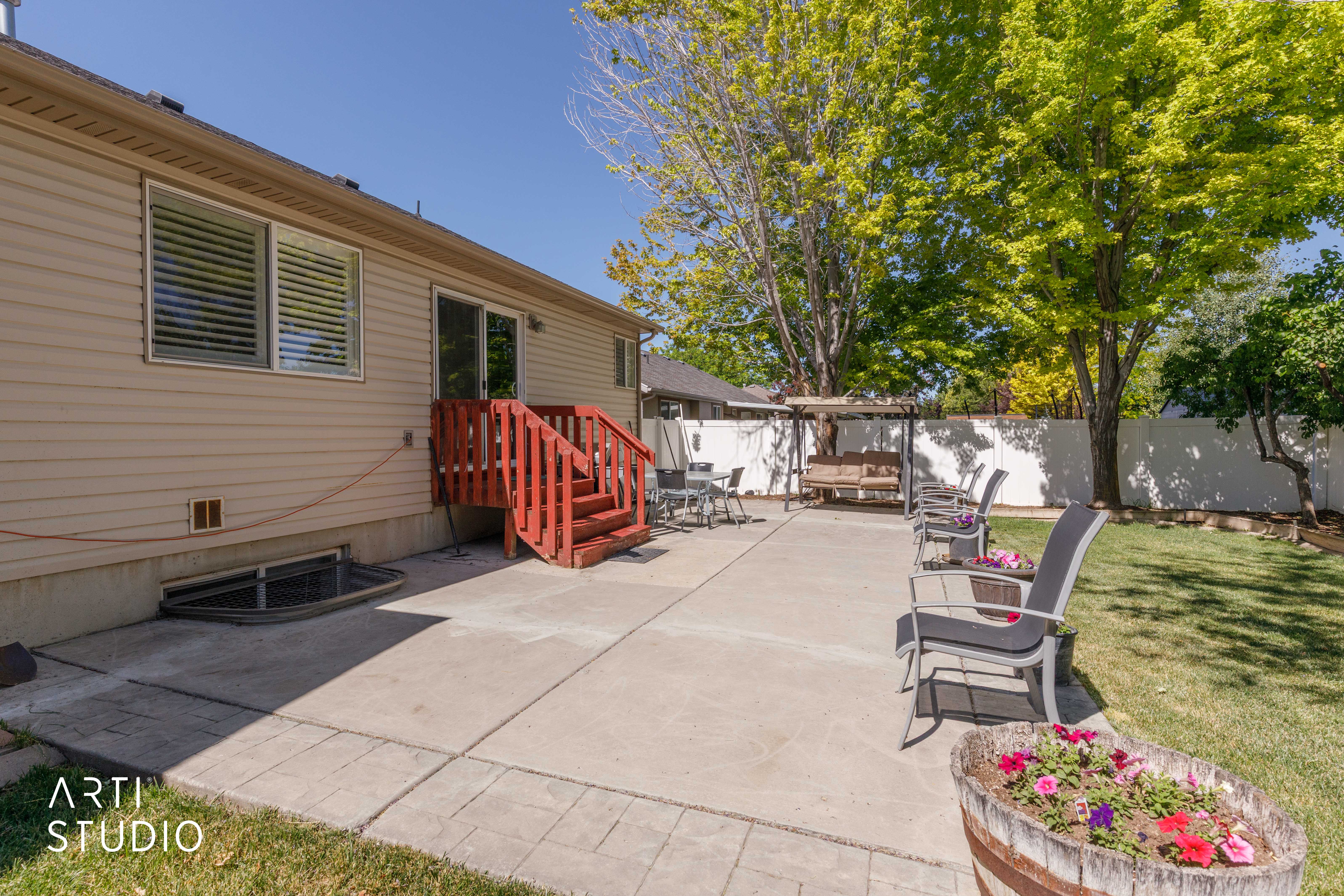 Expansive concrete patio area with a red-stained wood deck and stairway