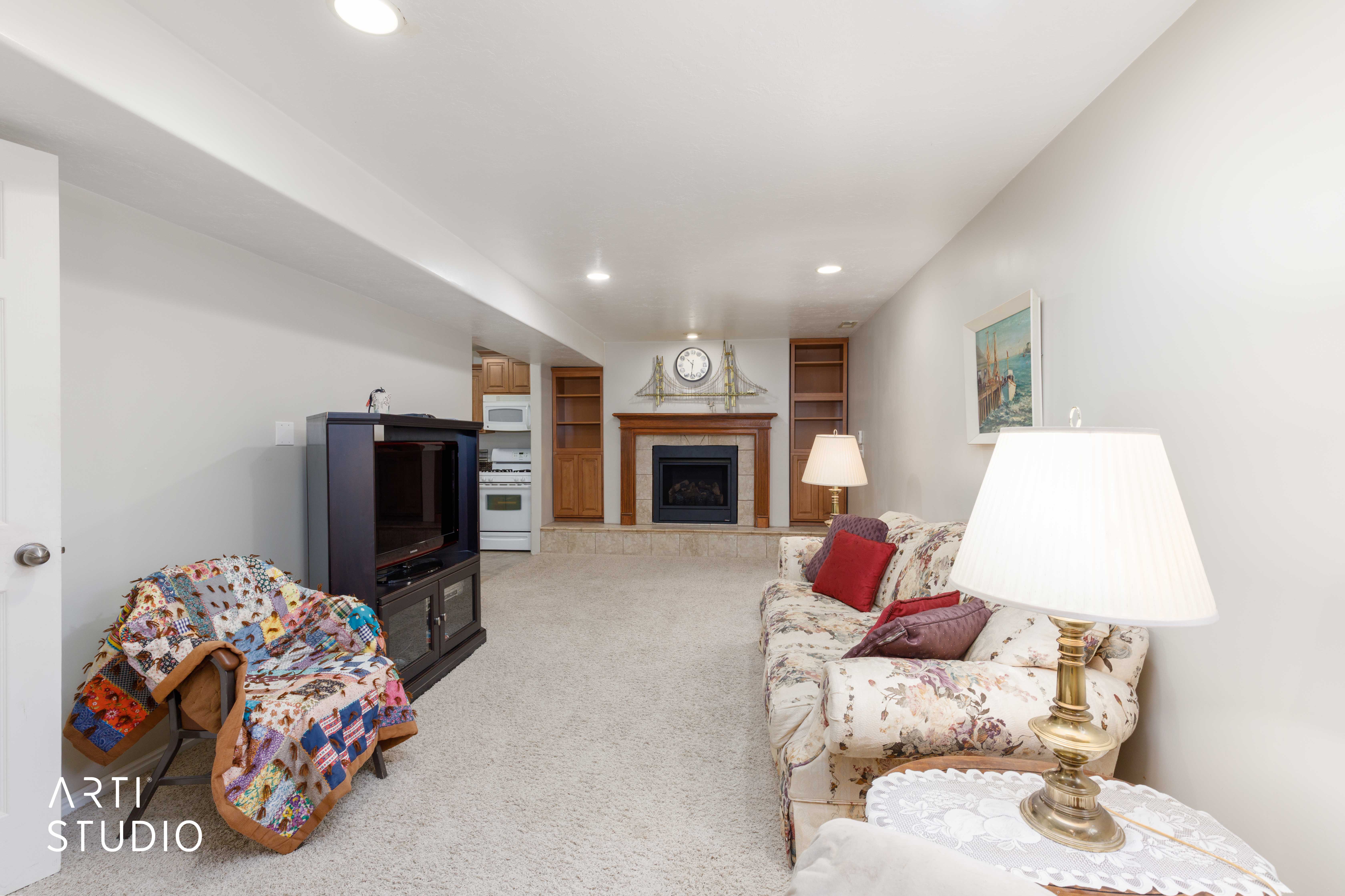 Recessed lighting illuminates a carpeted living space featuring a fireplace with a wood mantle and hearth, flanked by built-in shelving units