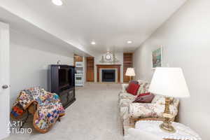 Recessed lighting illuminates a carpeted living space featuring a fireplace with a wood mantle and hearth, flanked by built-in shelving units