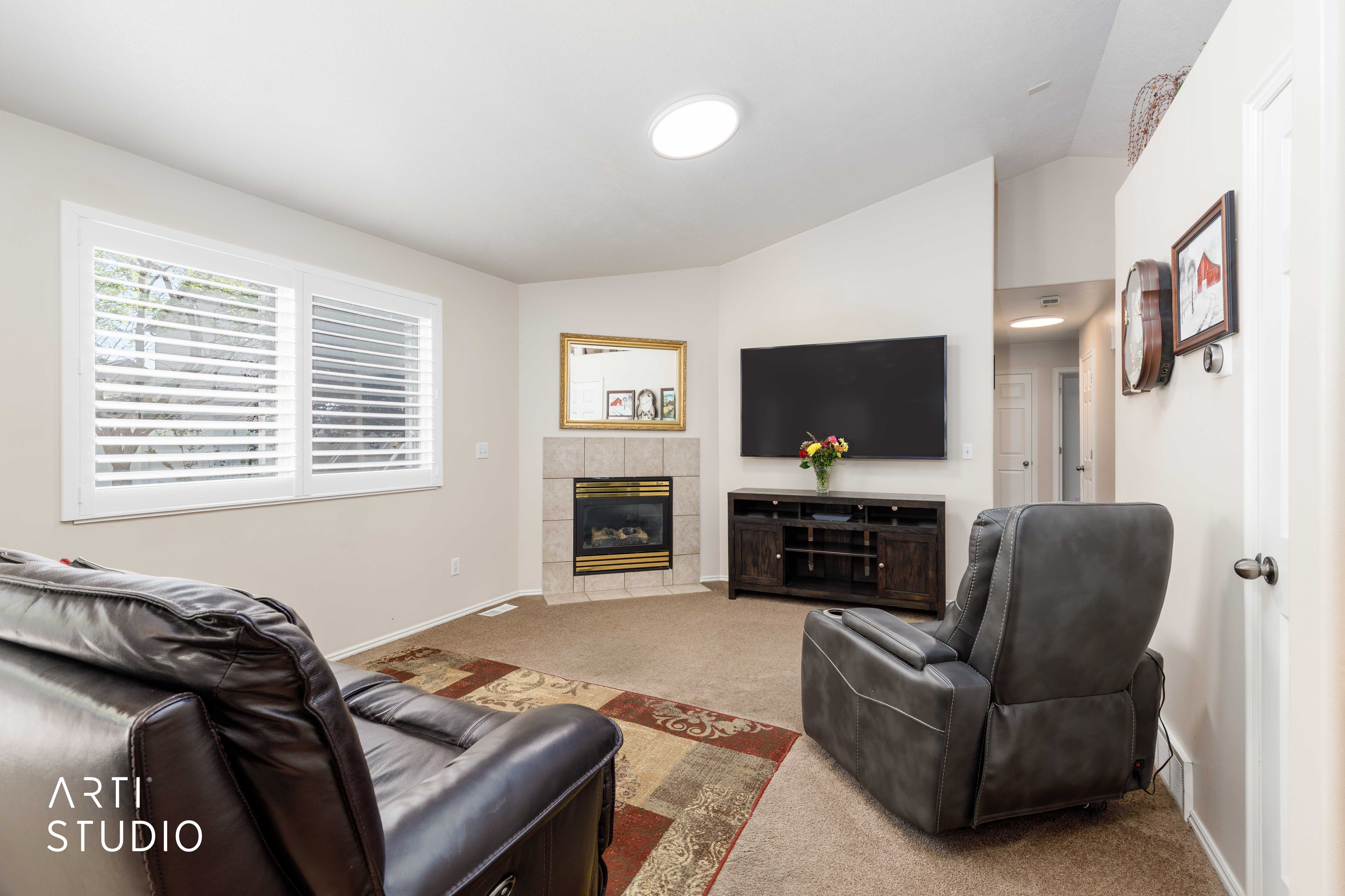 Living area with vaulted ceilings, a corner fireplace with stone tile surround, and plantation shutters