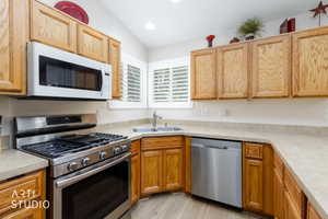 Kitchen featuring wood cabinetry, stainless steel appliances including a gas range and dishwasher, composite countertops, and wood-finish flooring