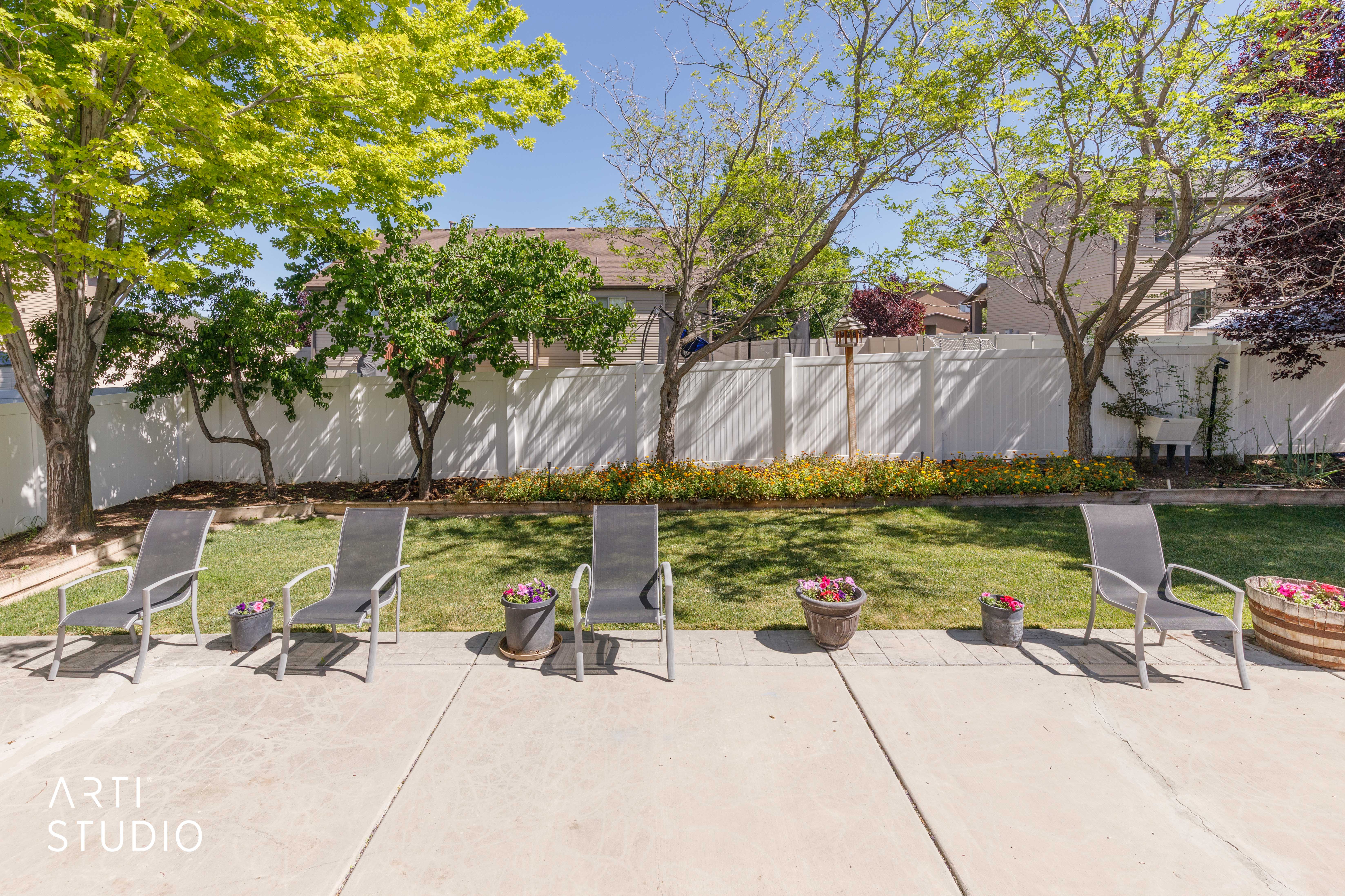 Spacious backyard featuring a concrete patio, a manicured lawn, mature trees, and a white privacy fence