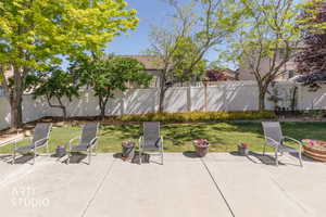 Spacious backyard featuring a concrete patio, a manicured lawn, mature trees, and a white privacy fence