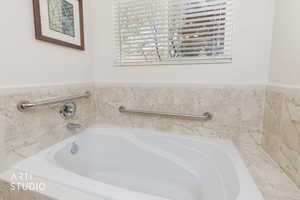 Soaking tub with chrome fixtures, surrounded by neutral-toned tiled walls, and accented by stainless steel grab bars