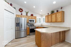 Kitchen featuring light wood-finish flooring, vaulted ceiling, recessed lighting, wood cabinetry, stainless steel appliances, and L-shaped counter space