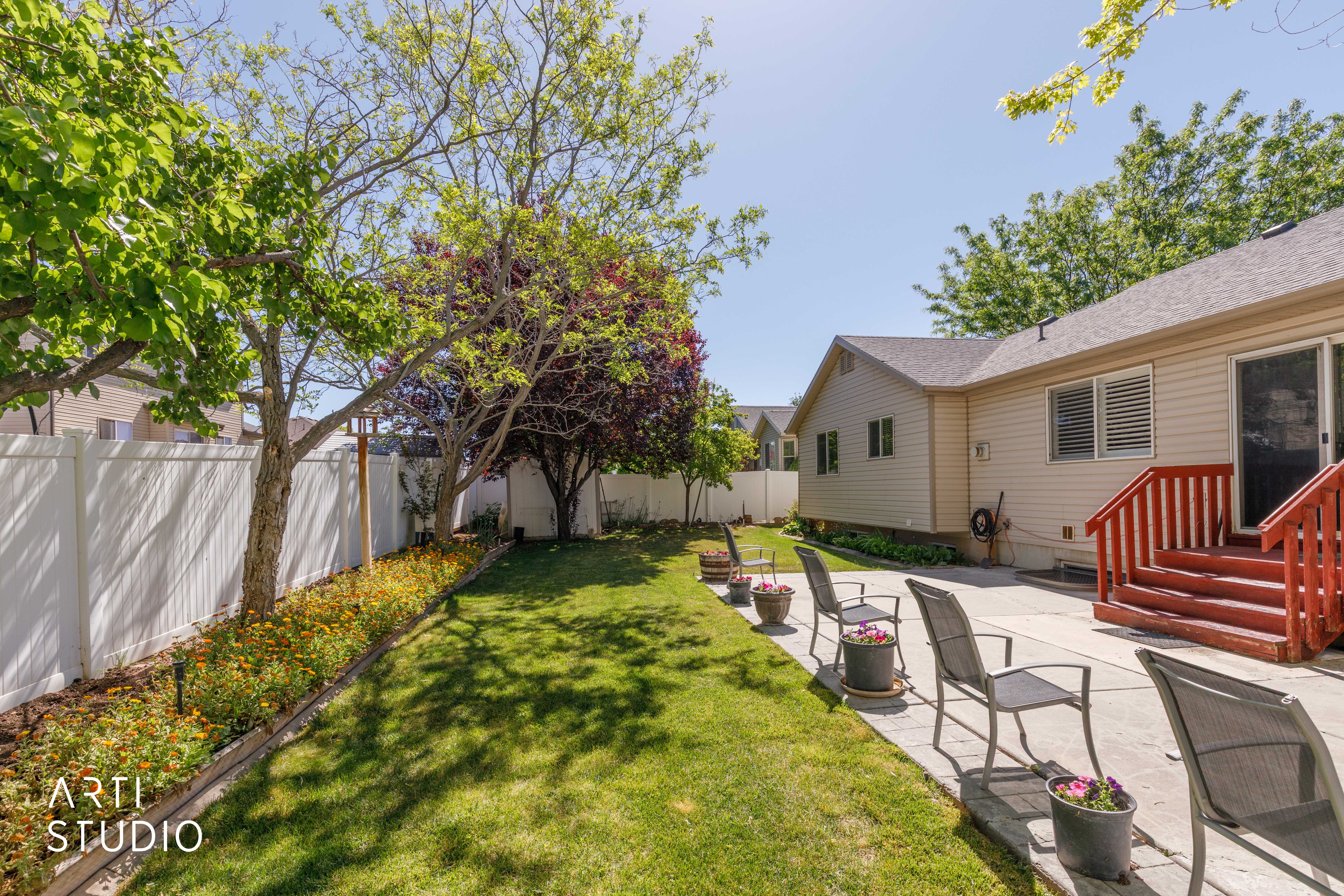 Expansive backyard with a manicured lawn, established trees, and a white privacy fence