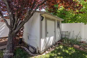 Freestanding storage shed with paneled siding and a window, situated alongside a white privacy fence