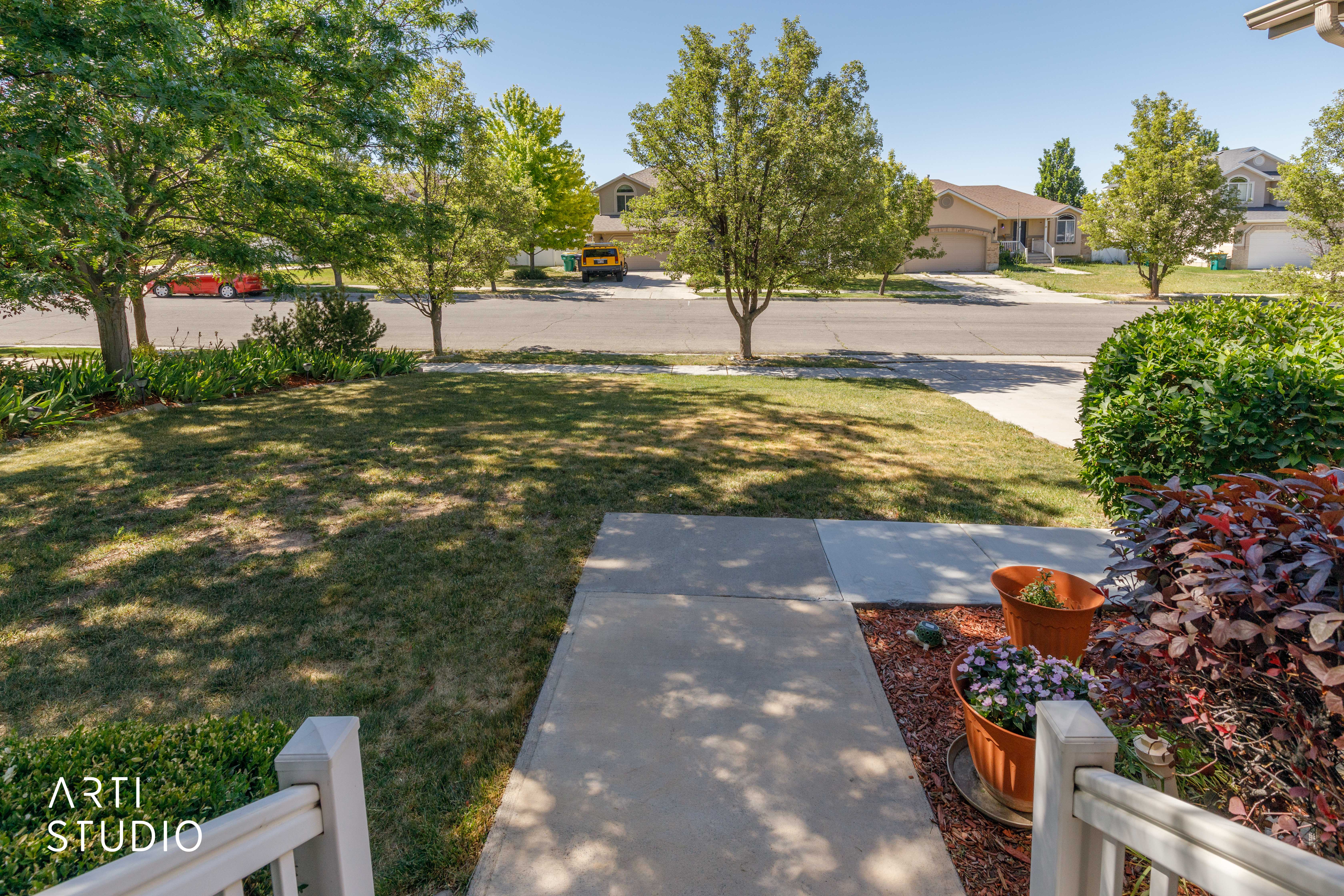 Front yard featuring a concrete pathway, green lawn, mature trees, and landscaping with shrubs and ground cover