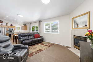 Living area featuring a fireplace with a tile surround, carpet flooring, and a kitchen visible in the background