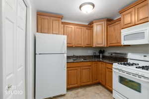 Kitchen featuring wood-finish cabinetry, granite-style countertops, an overhead microwave, a gas range, and a double-door refrigerator