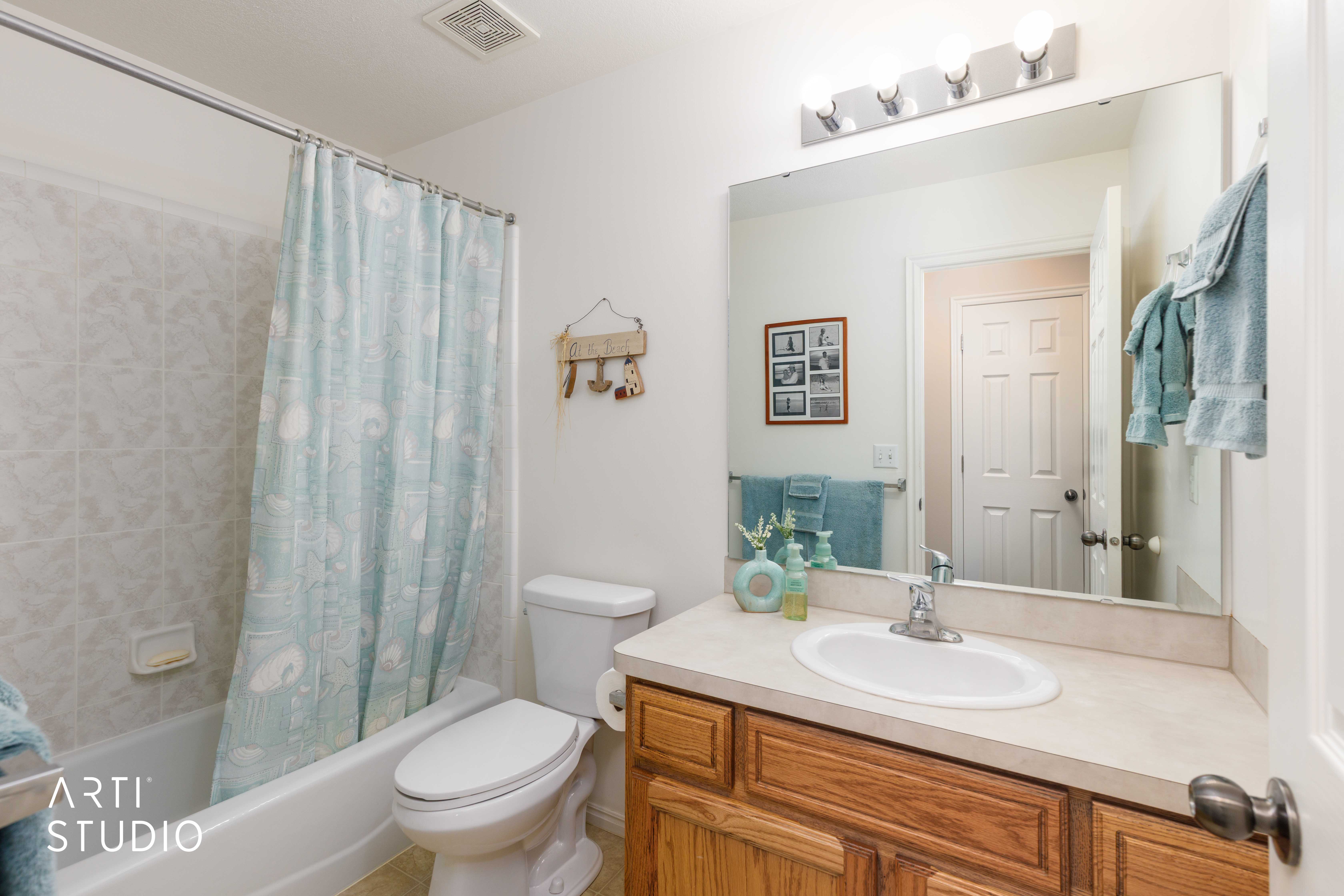 Full bathroom featuring a white tub-shower combination with tiled surround, a toilet, and a wood-finish vanity with an integrated sink and light-toned countertop