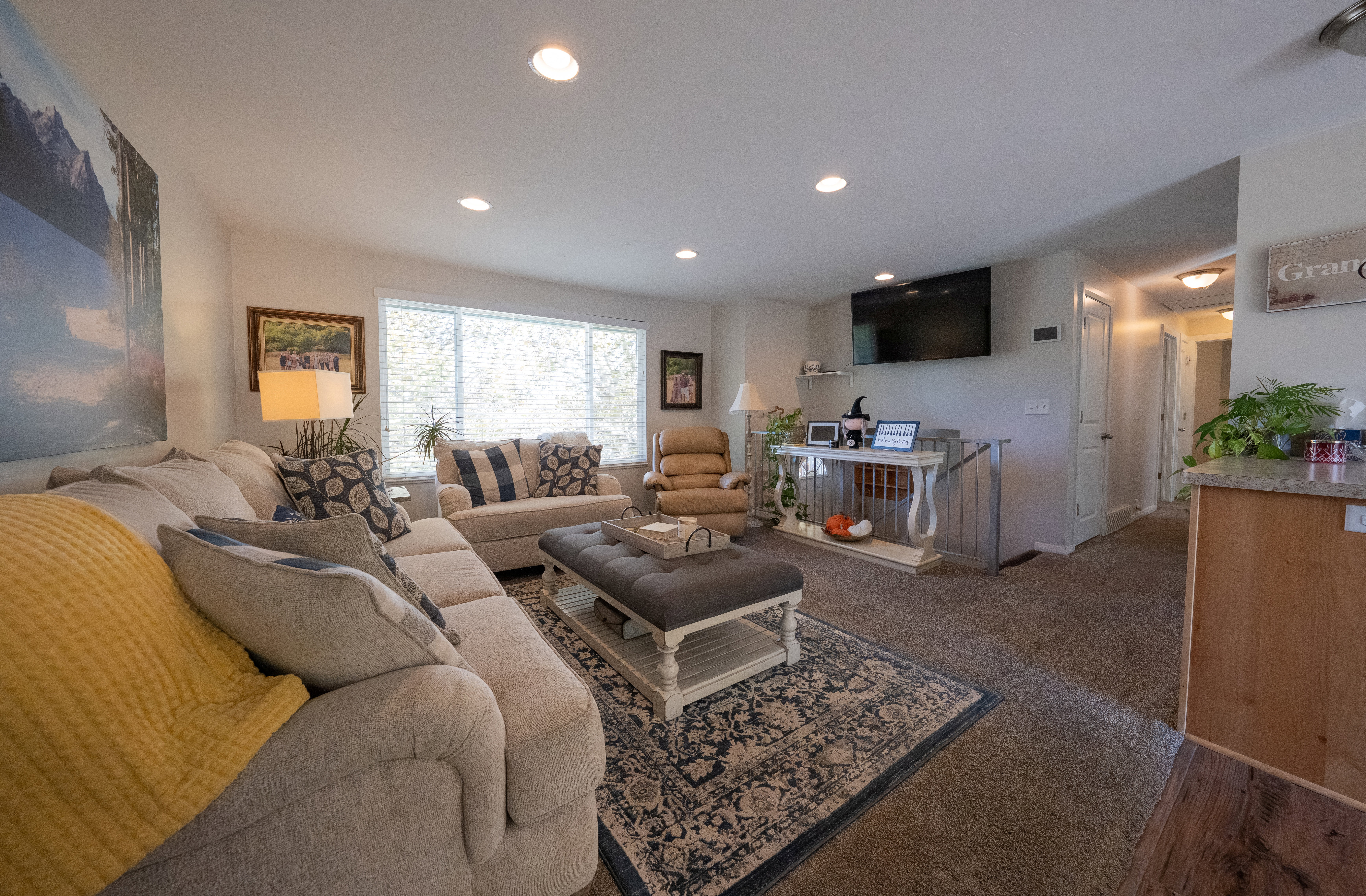 Spacious living area featuring recessed lighting, a large window with blinds, and carpeted flooring