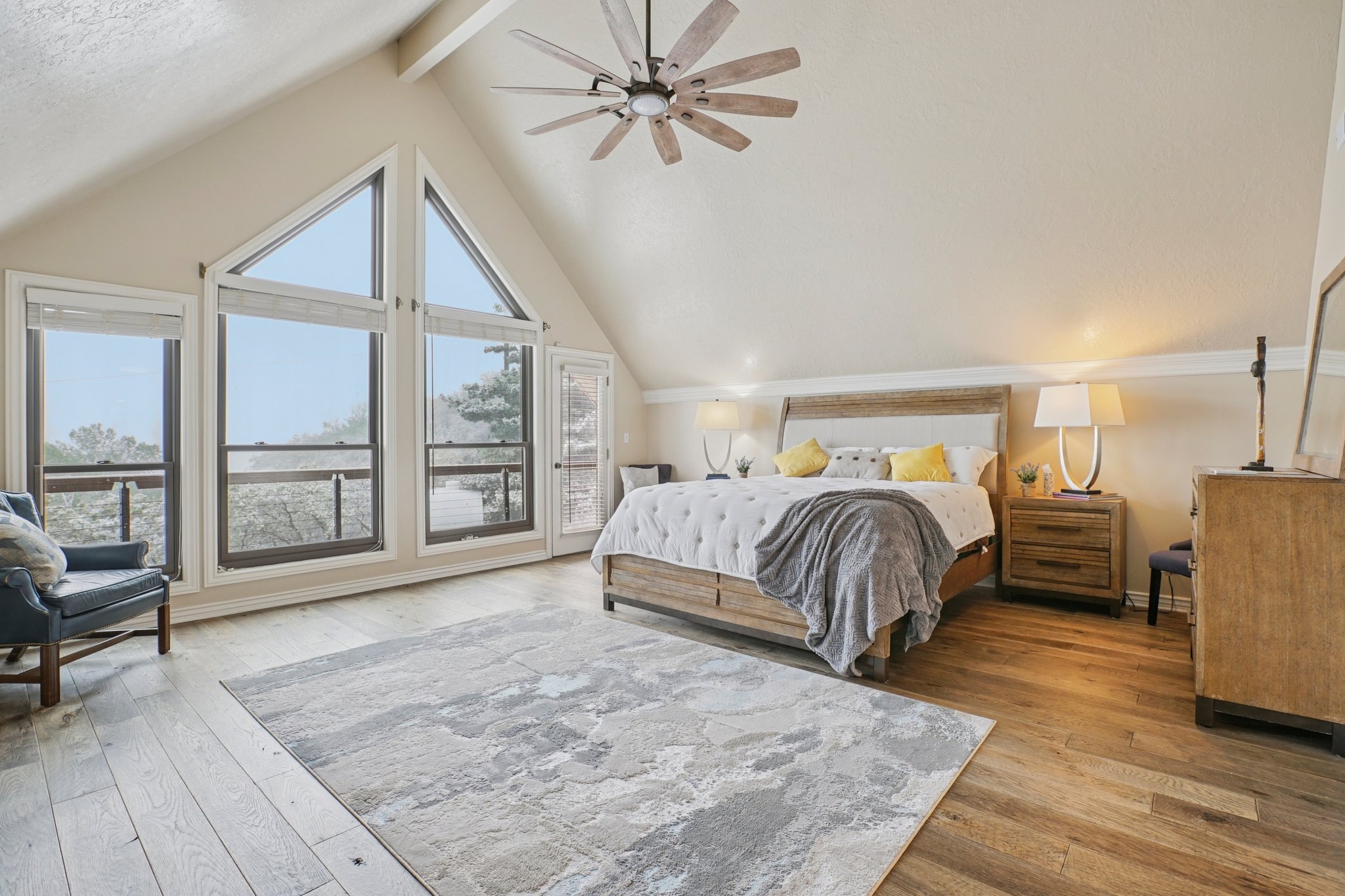 Vaulted ceilings featuring a ceiling fan, a wall of windows including two triangular windows, wood-finish flooring, and crown molding
