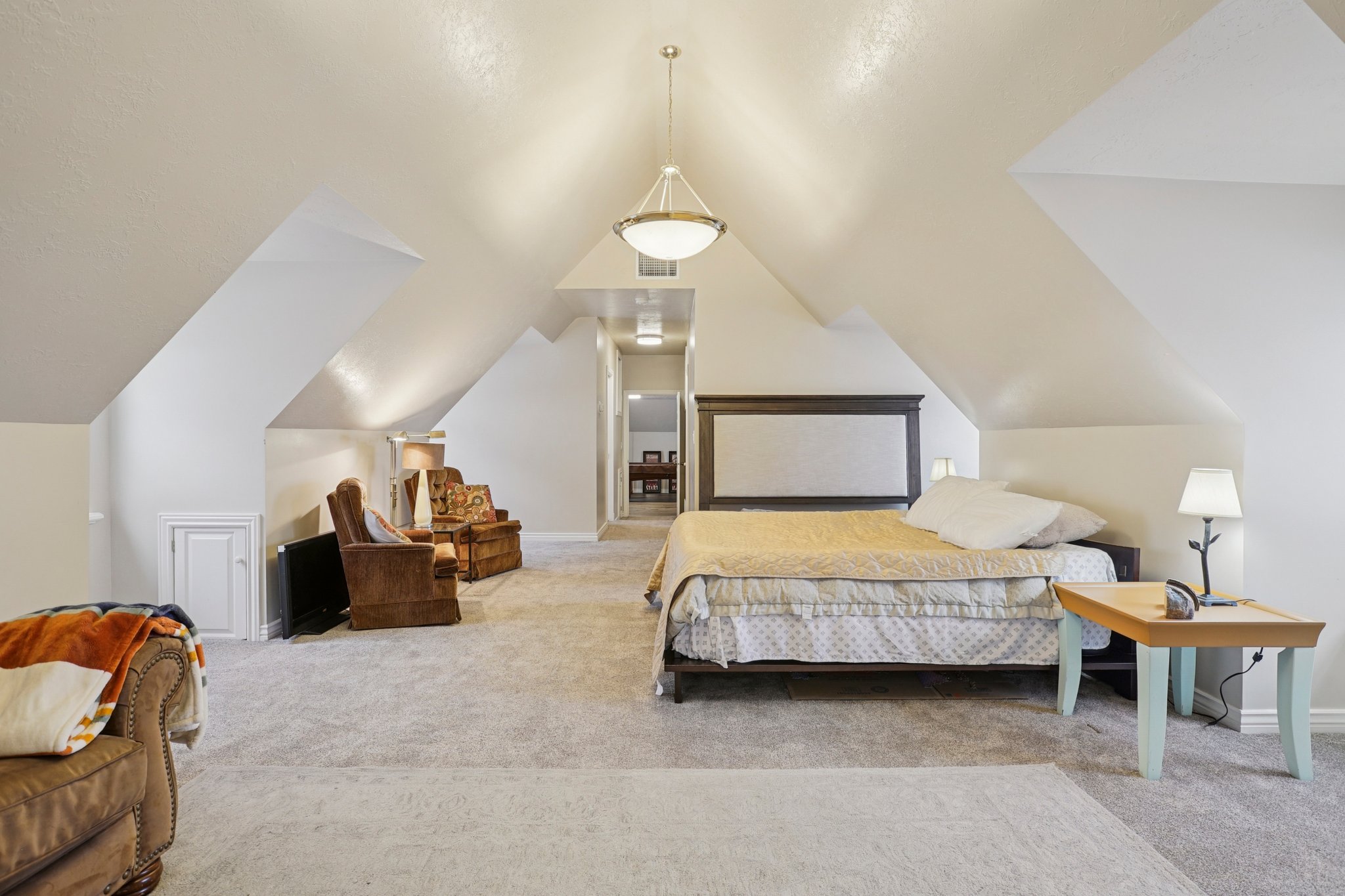 Vaulted ceiling room featuring light gray carpeting, neutral wall colors, and a central pendant light fixture
