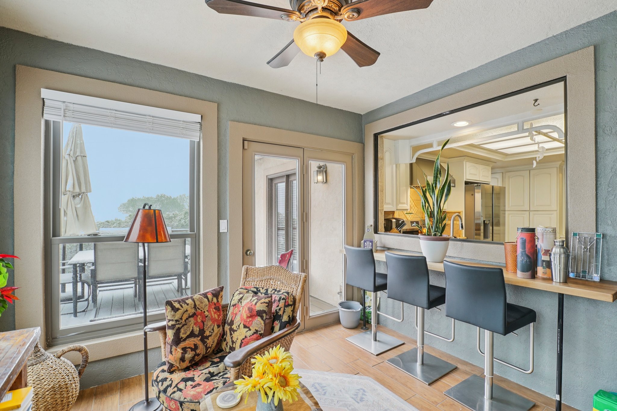 Open-concept pass-through bar with three integrated stools, wood-finish flooring, a ceiling fan with integrated lighting, and a glass-paneled door opening to an exterior patio