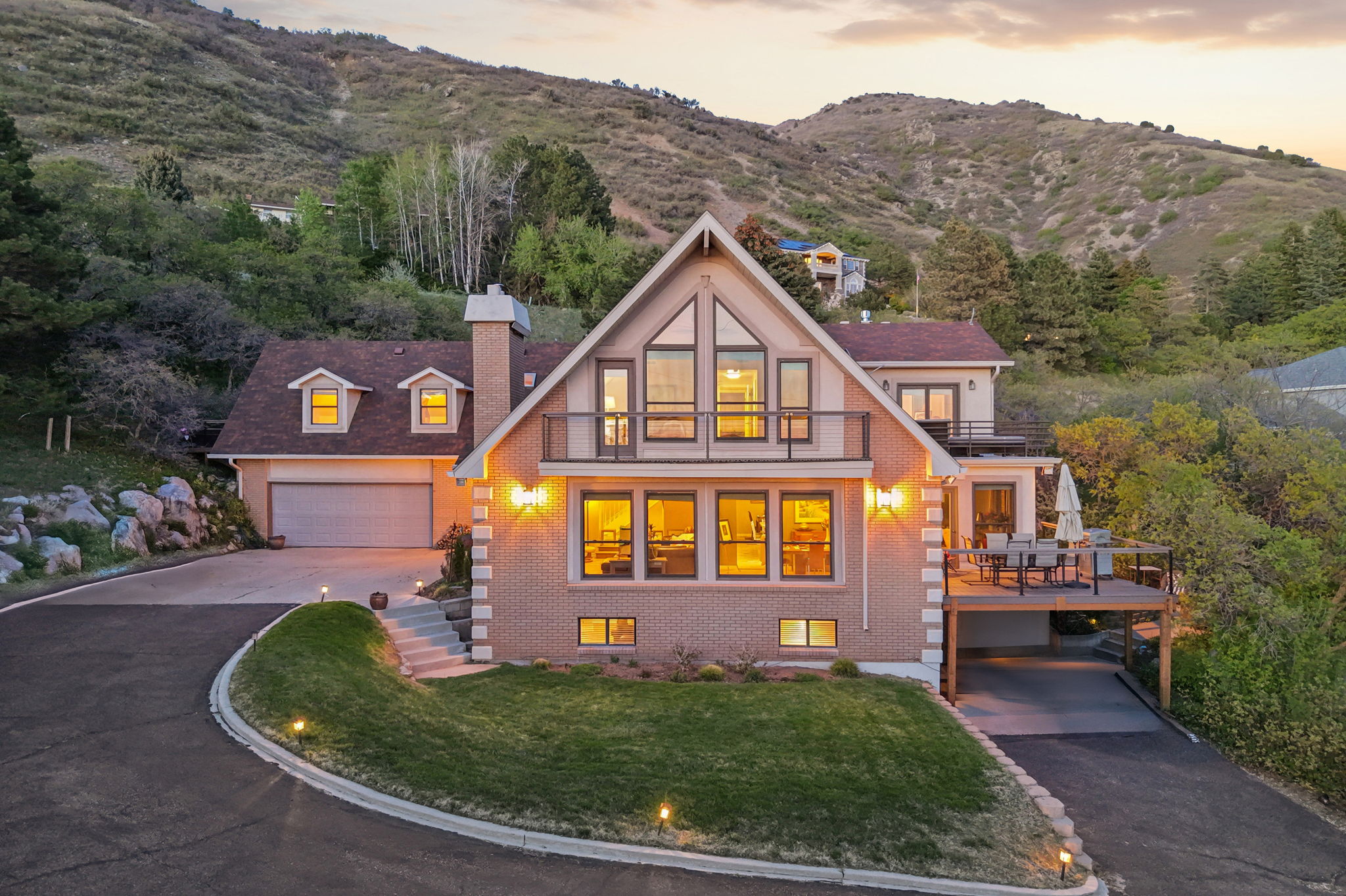 Hillside residence featuring a brick and siding exterior, multi-pane windows, a prominent A-frame architectural element, an attached two-car garage, and an elevated outdoor deck