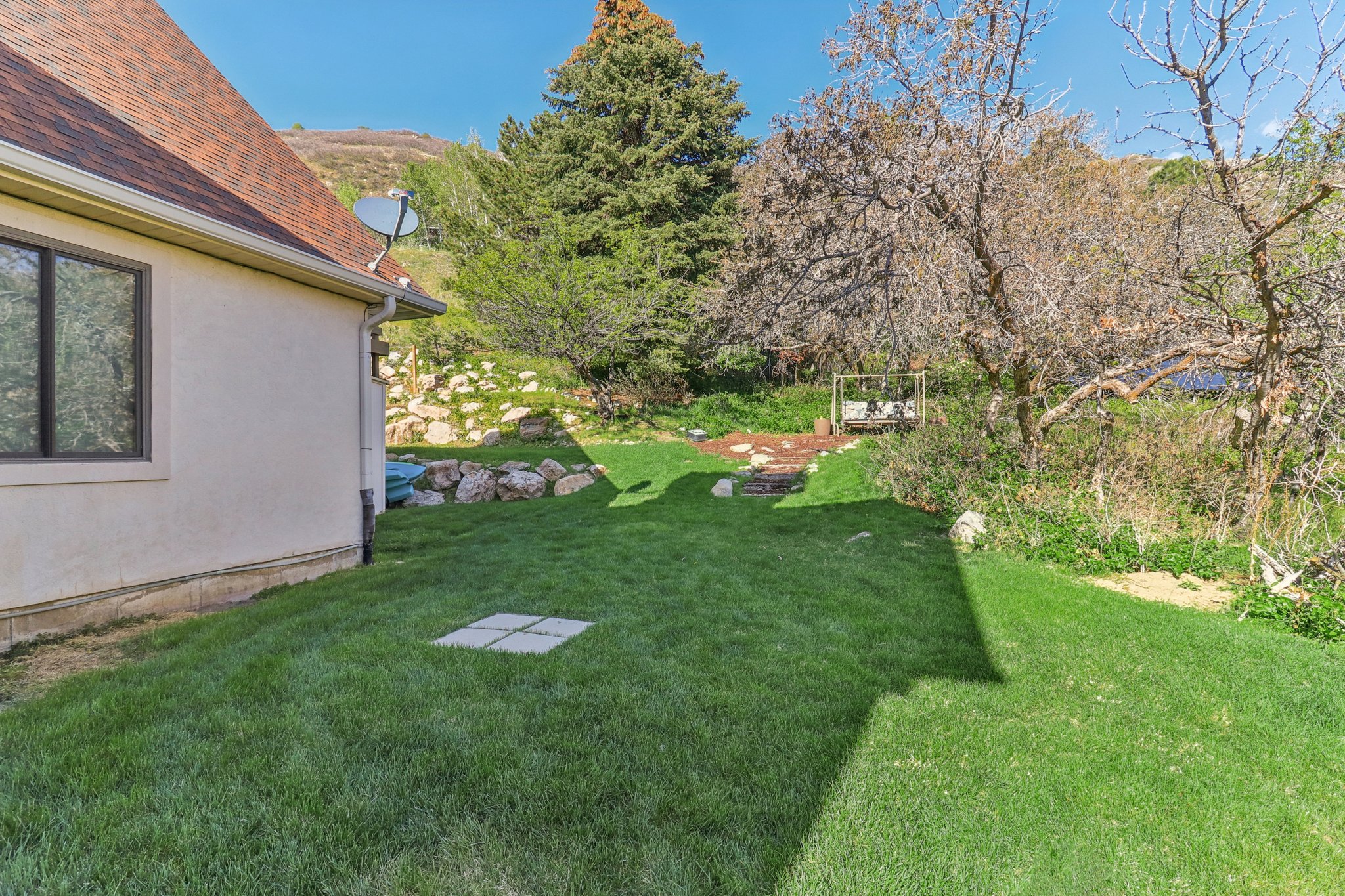 Expansive green lawn with a gradual incline, bordered by natural rock landscaping and mature trees