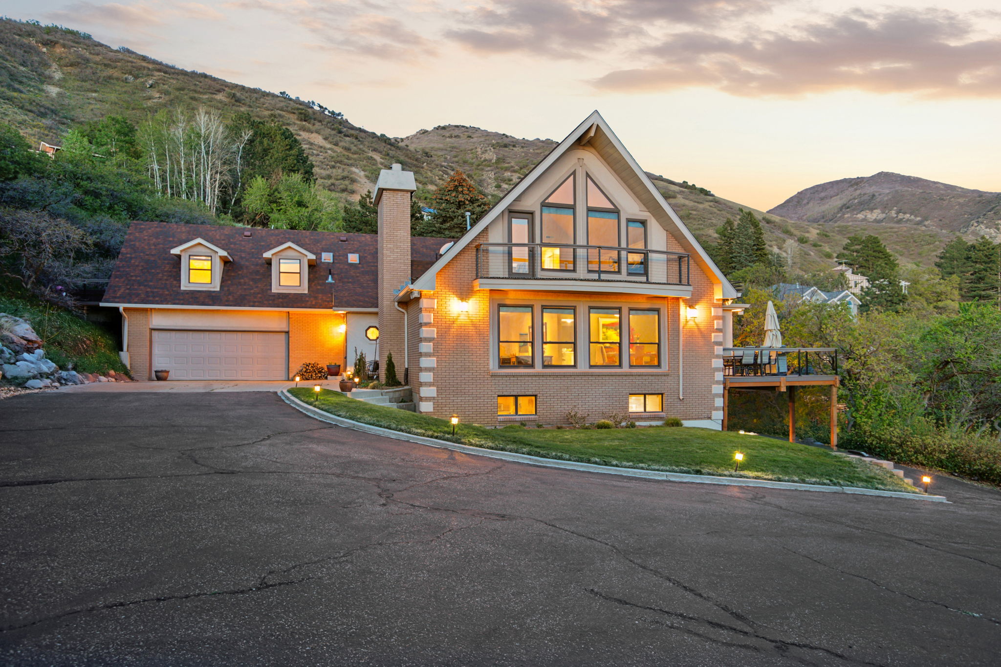 Brick facade residence featuring an attached garage, prominent gable roofline, upper-level balcony, and a multi-level deck