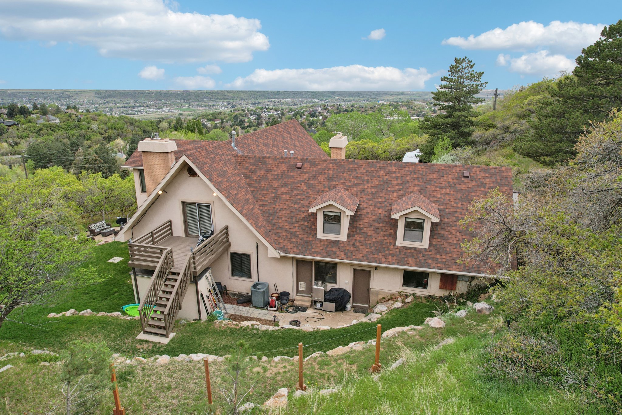 Multi-level residence featuring a brown shingle roof, twin dormer windows, and a large wooden deck with exterior stairs