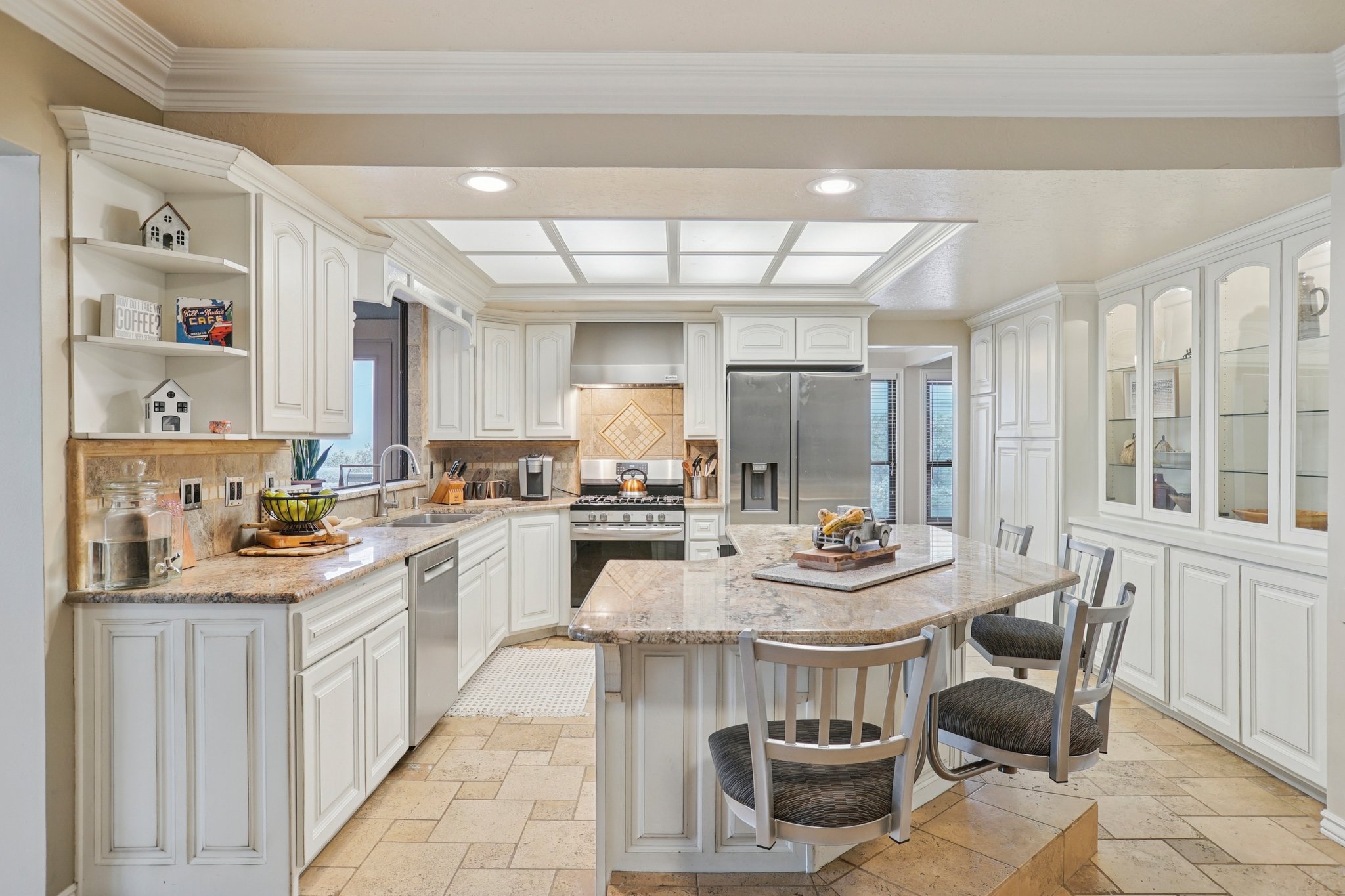 Spacious kitchen featuring an expansive island with seating, white cabinetry, integrated stainless steel appliances, tiled flooring, and recessed lighting