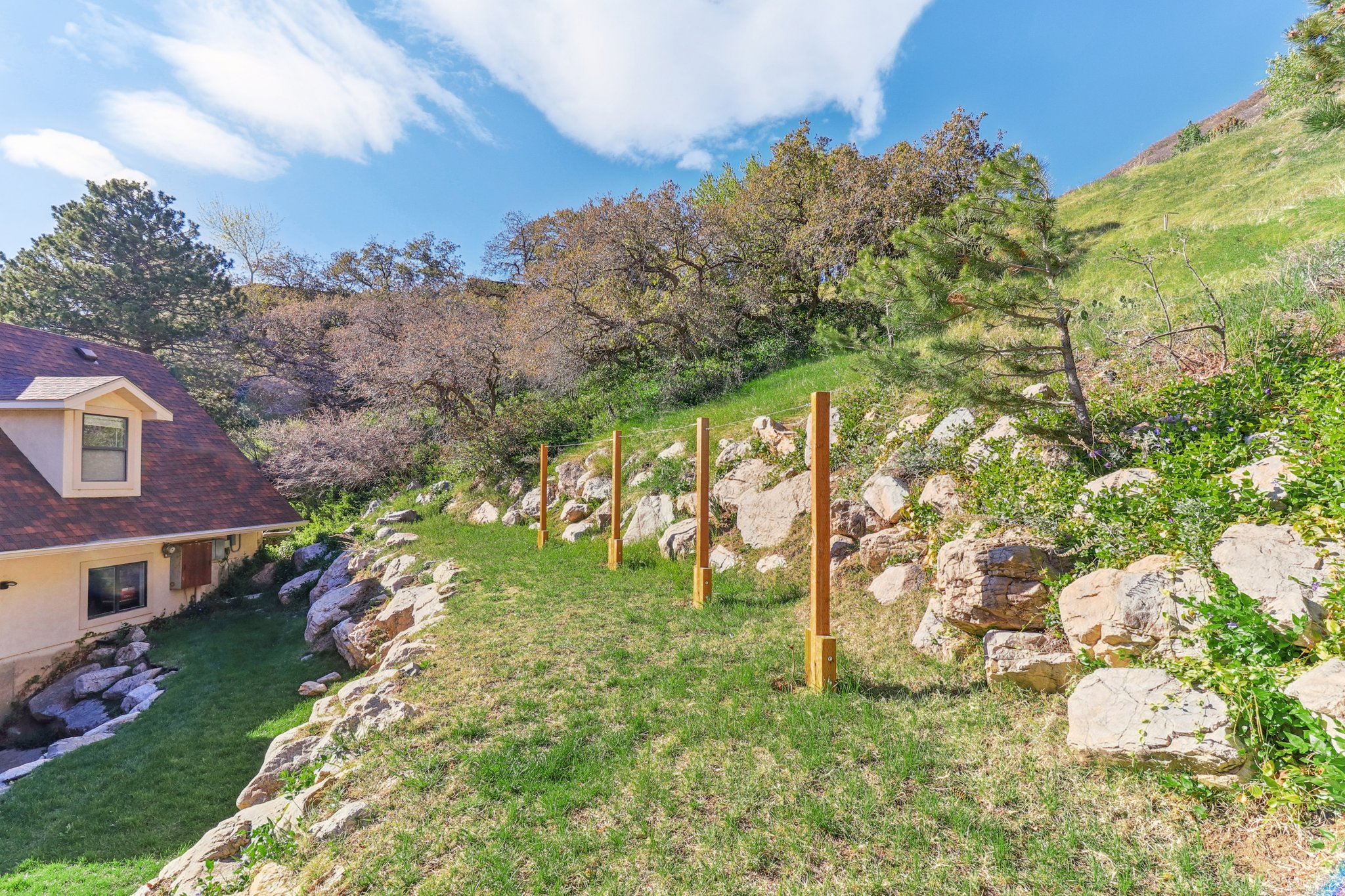 Sloped backyard featuring natural rock retaining walls, mature trees, and an established green lawn