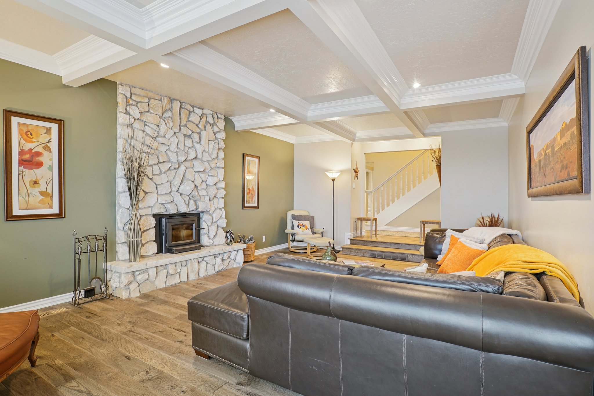 Living area showcasing a stone fireplace with wood-burning insert, wood-finish flooring, coffered ceiling, and recessed lighting